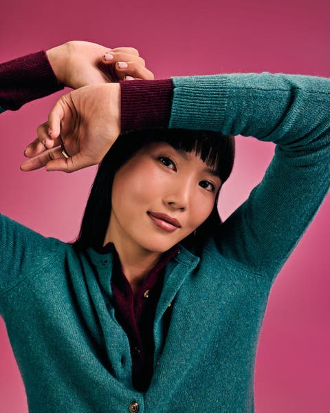 Woman in a teal knit cardigan with arms raised.