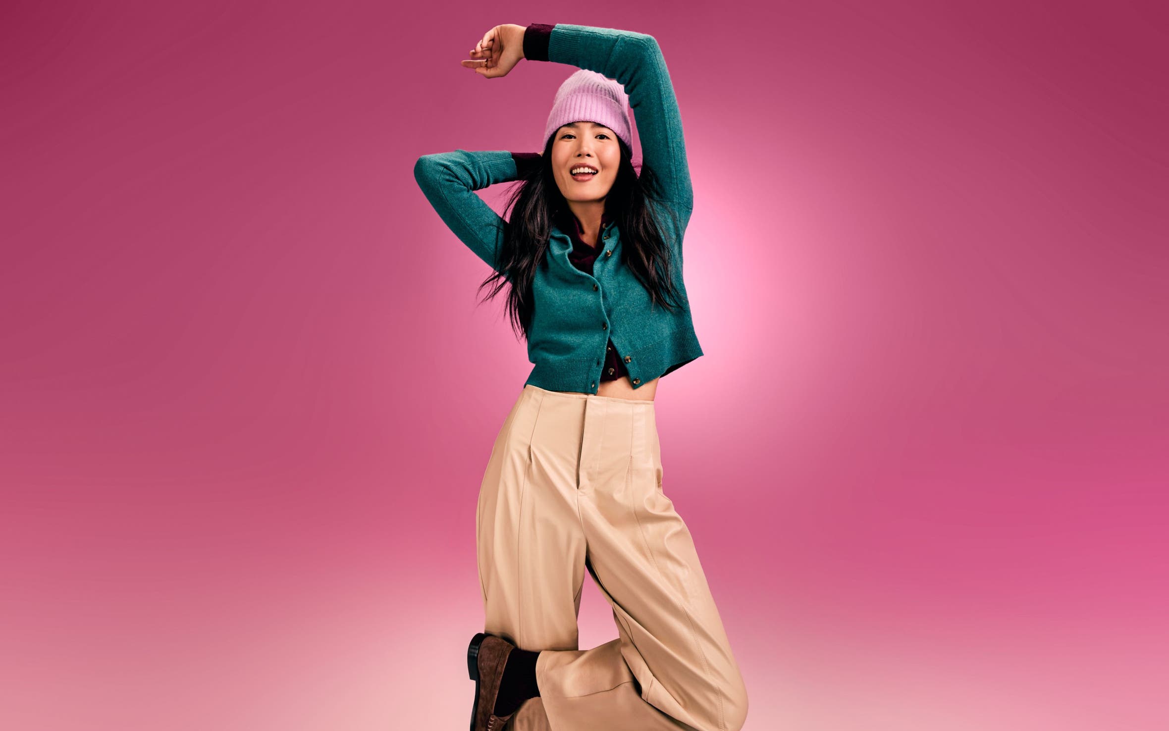 A woman wearing a teal cardigan, pink beanie and tan pants. 