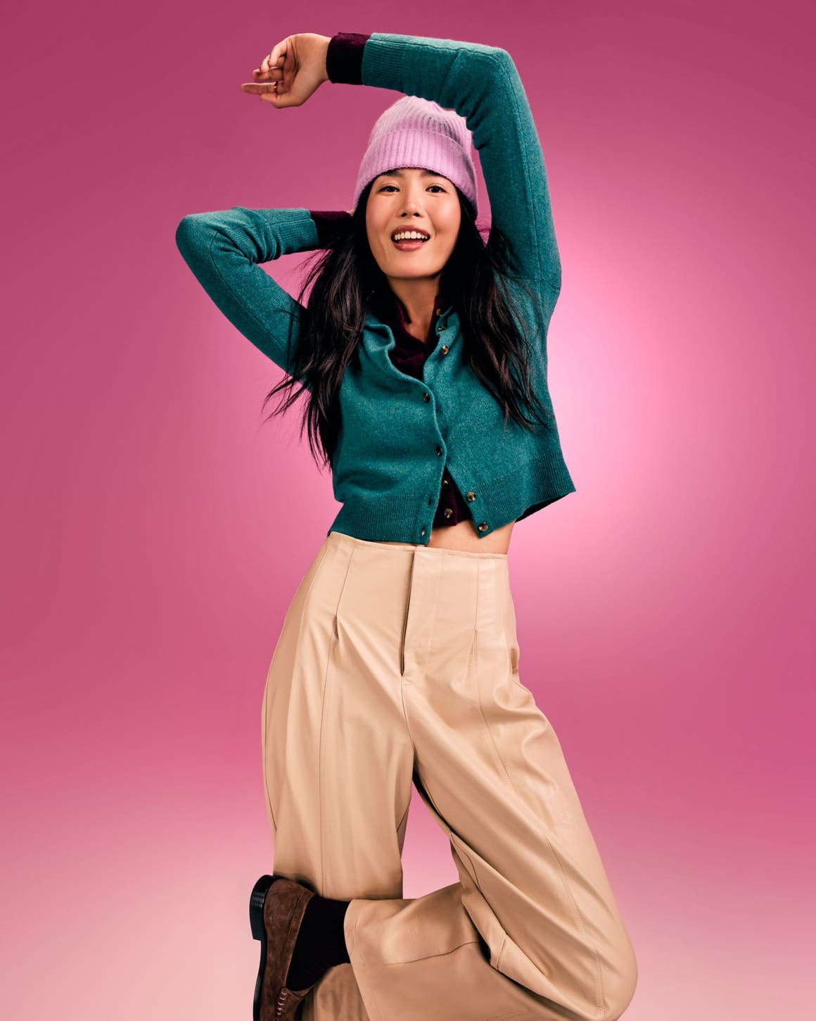 A woman wearing a teal cardigan, pink beanie and tan pants. 