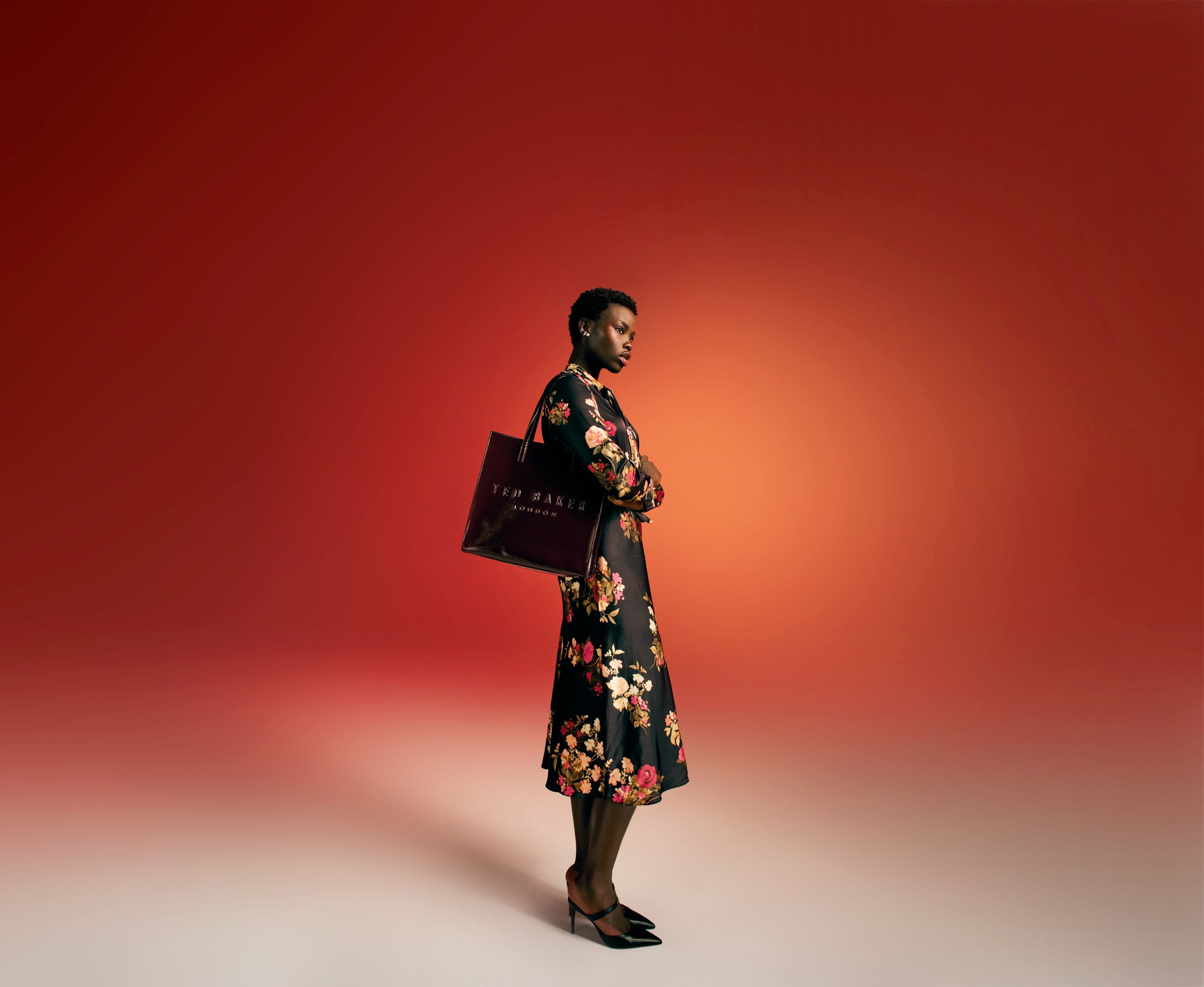 A woman wearing a floral-print dress and heels carries a black handbag. 