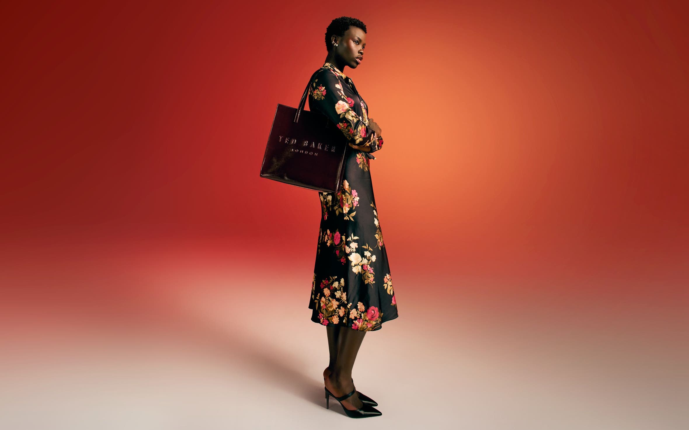 A woman wearing a floral-print dress and heels carries a black handbag. 