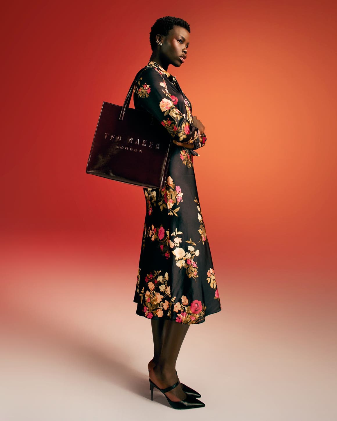 A woman wearing a floral-print dress and heels carries a black handbag. 
