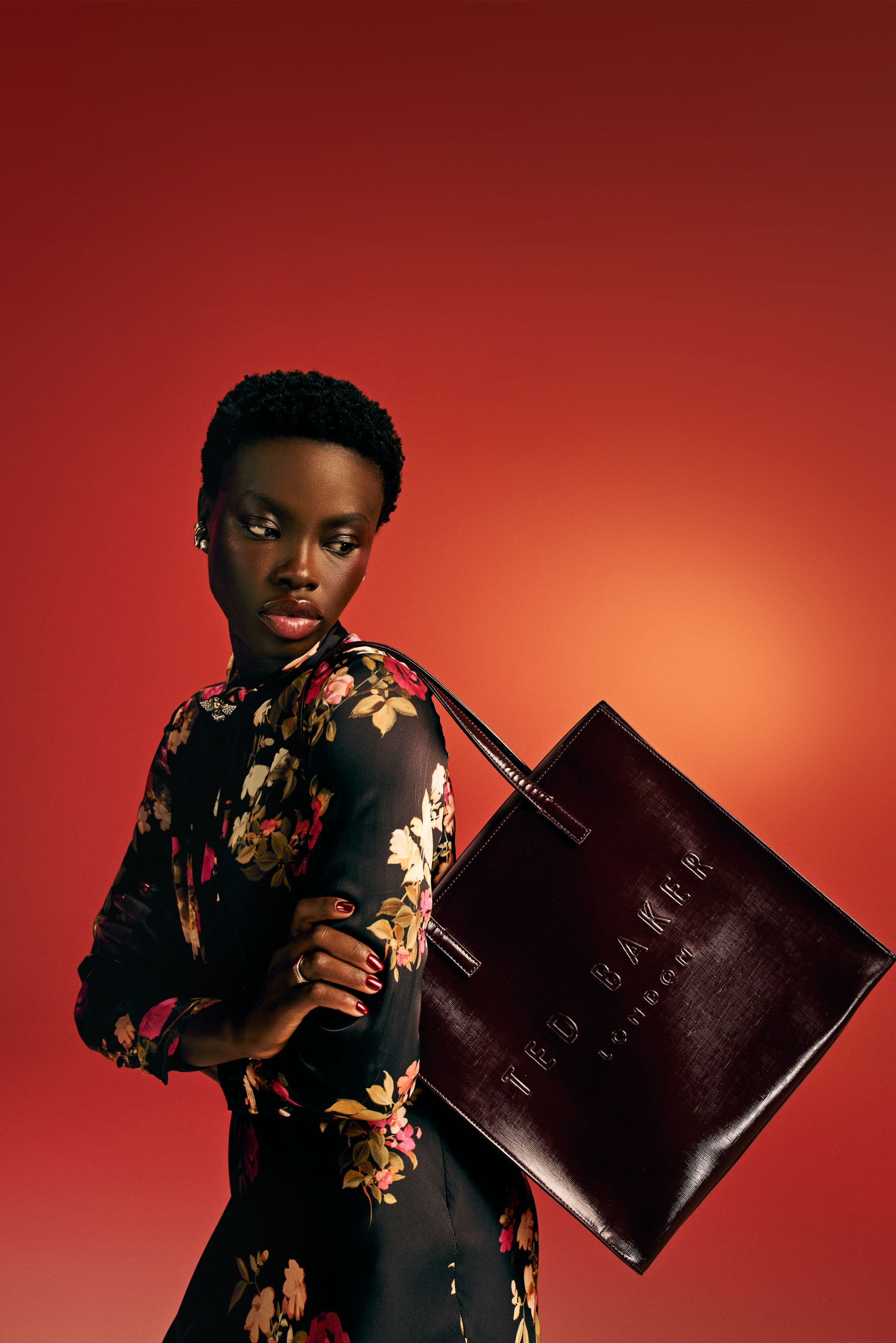 Woman in a black floral dress with a burgundy tote.