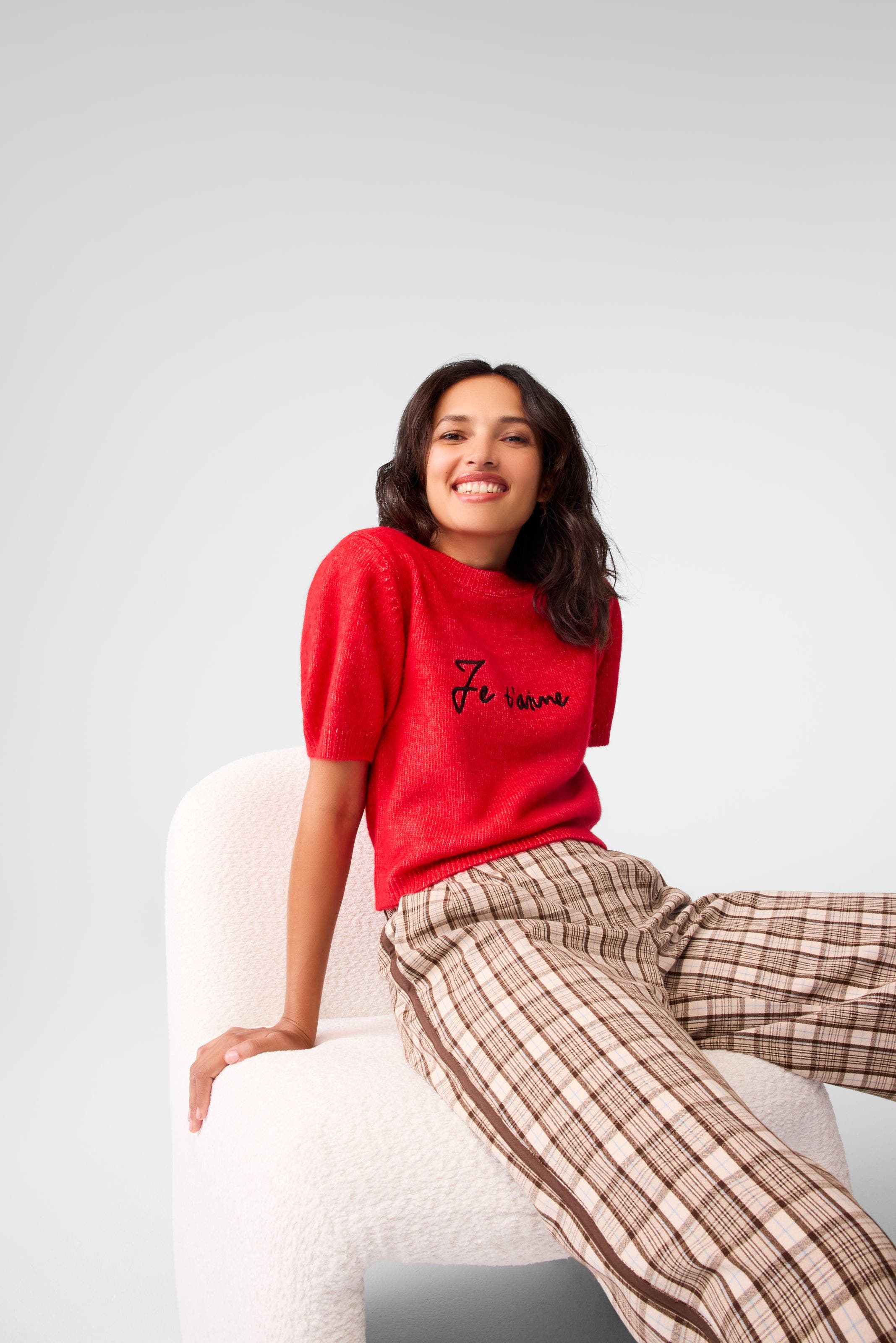 A woman wearing a red embroidered sweater and plaid pants. 