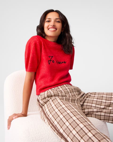 A woman wearing a red embroidered sweater and plaid pants.