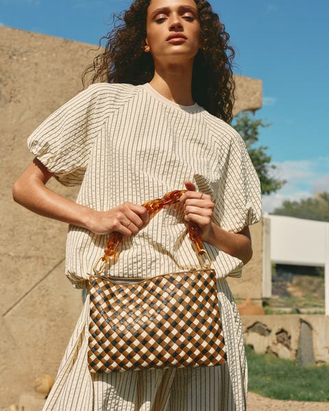 A woman wearing a striped top and skirt holding a woven handbag.
