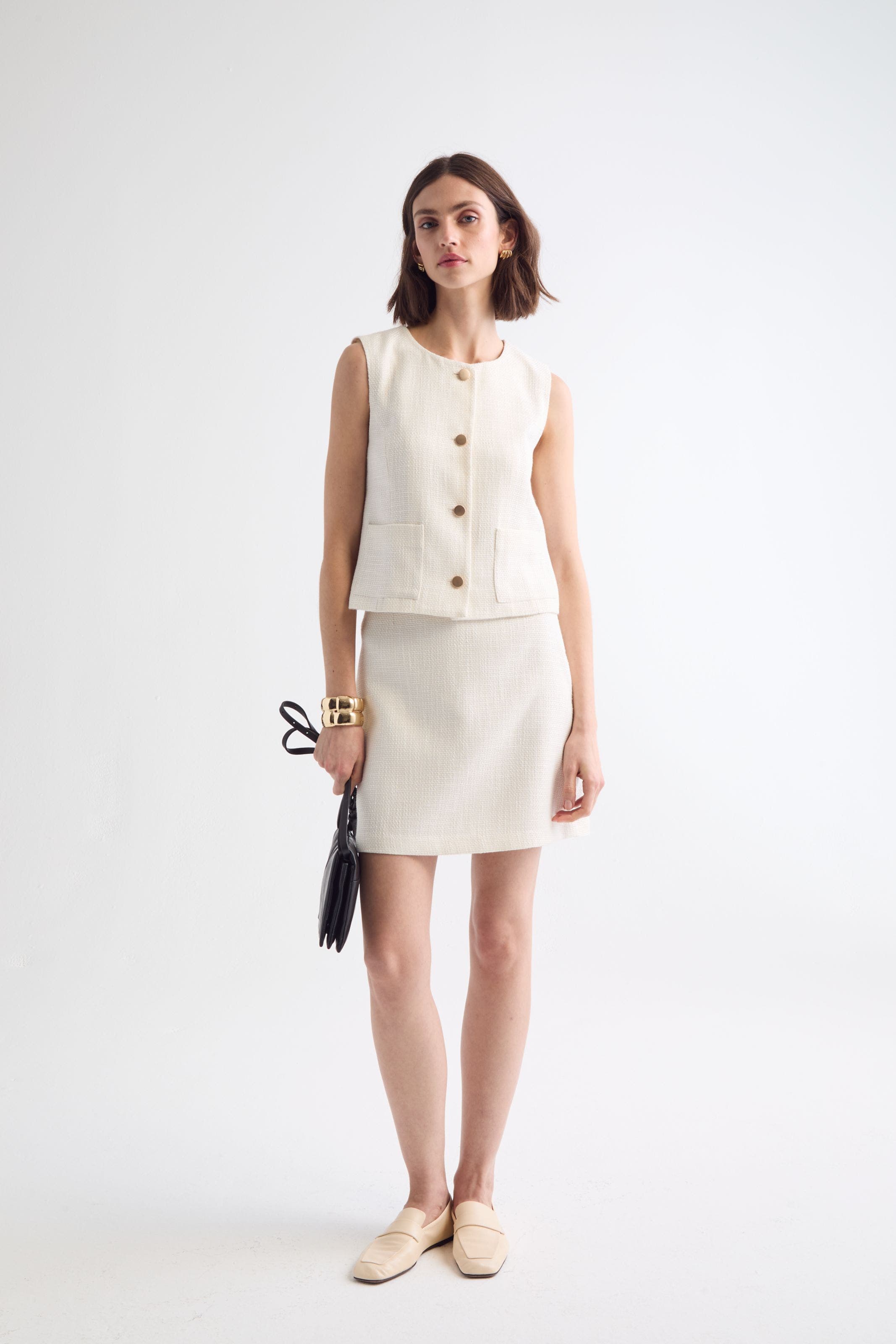 Woman wearing a matching cream colored vest and skiirt set.