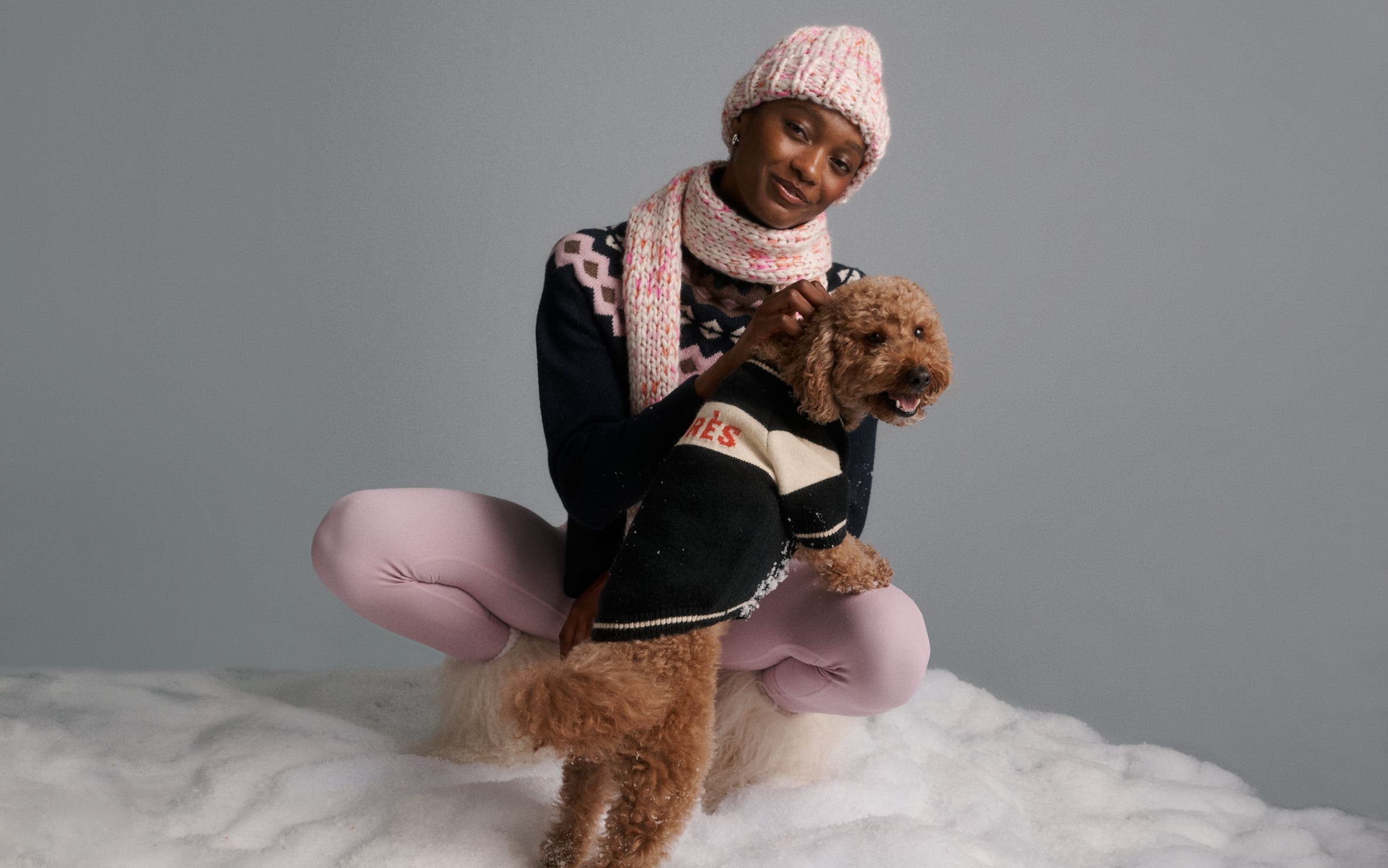 A woman wearing outerwear with a dog in a sweater.