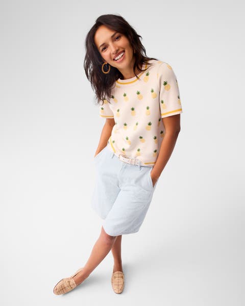 A woman wearing a printed top with Bermuda shorts and loafers. 