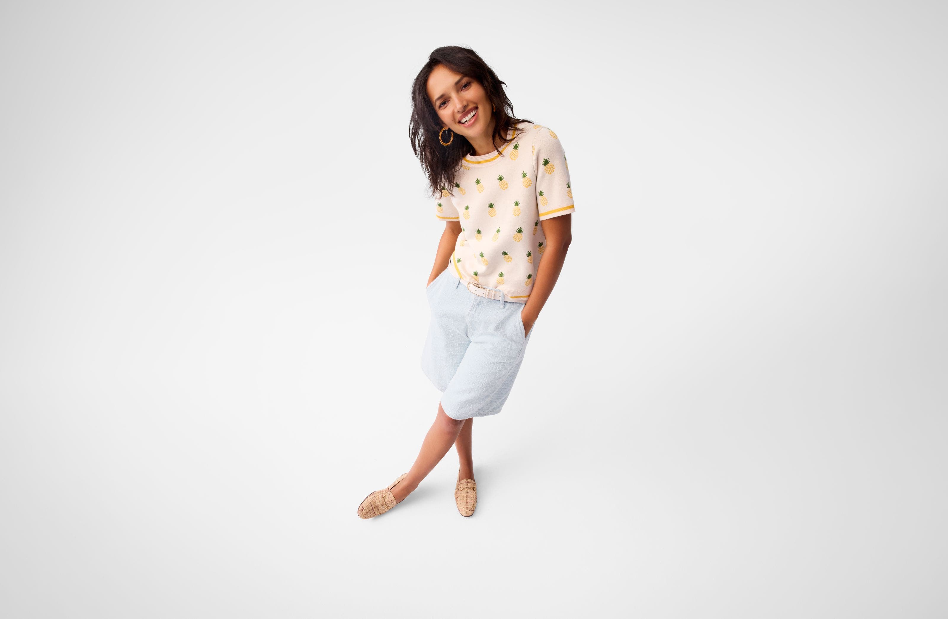 A woman wearing a printed top, shorts and loafers.