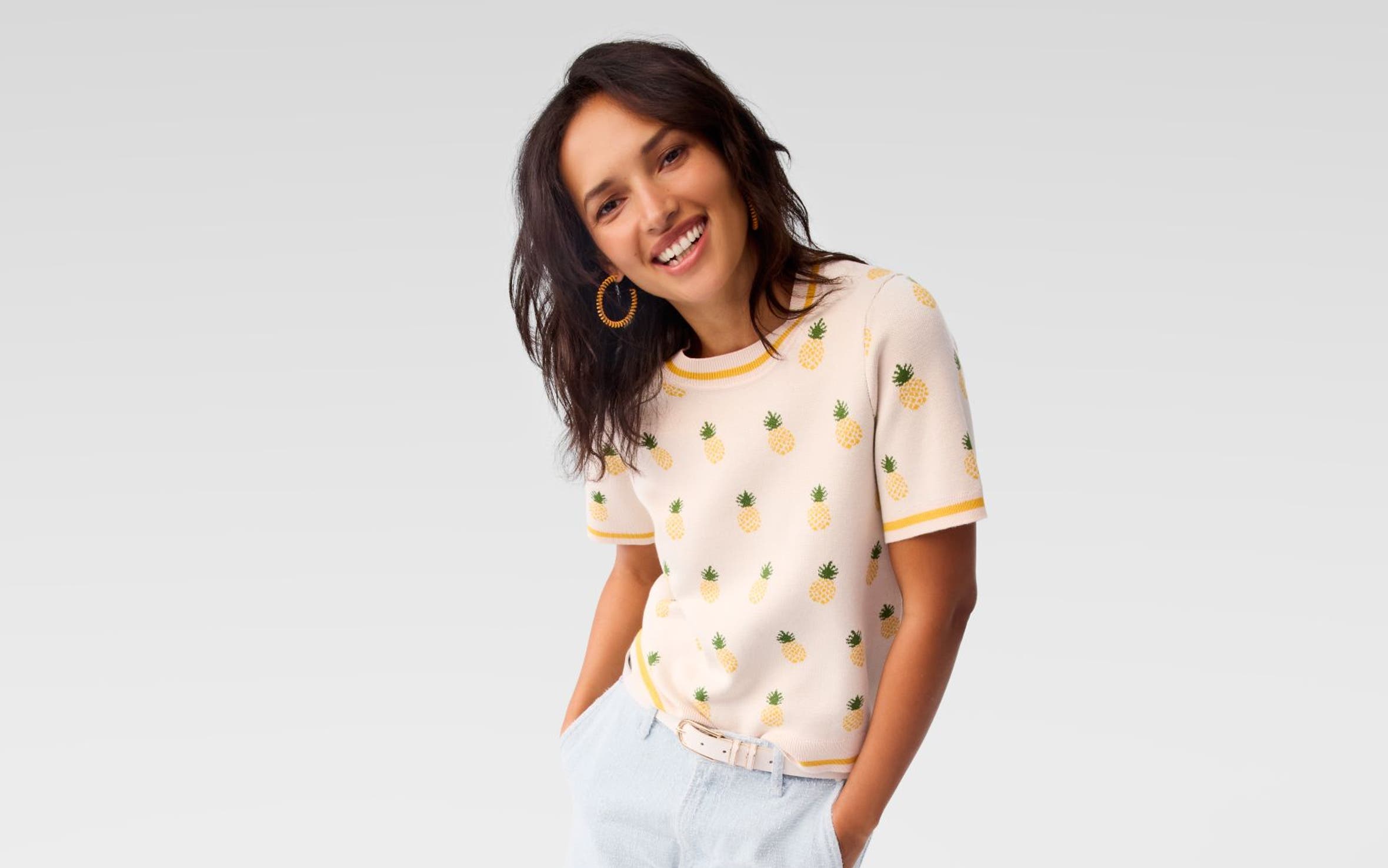 A woman wearing a knit top with a pineapple pattern and blue shorts.