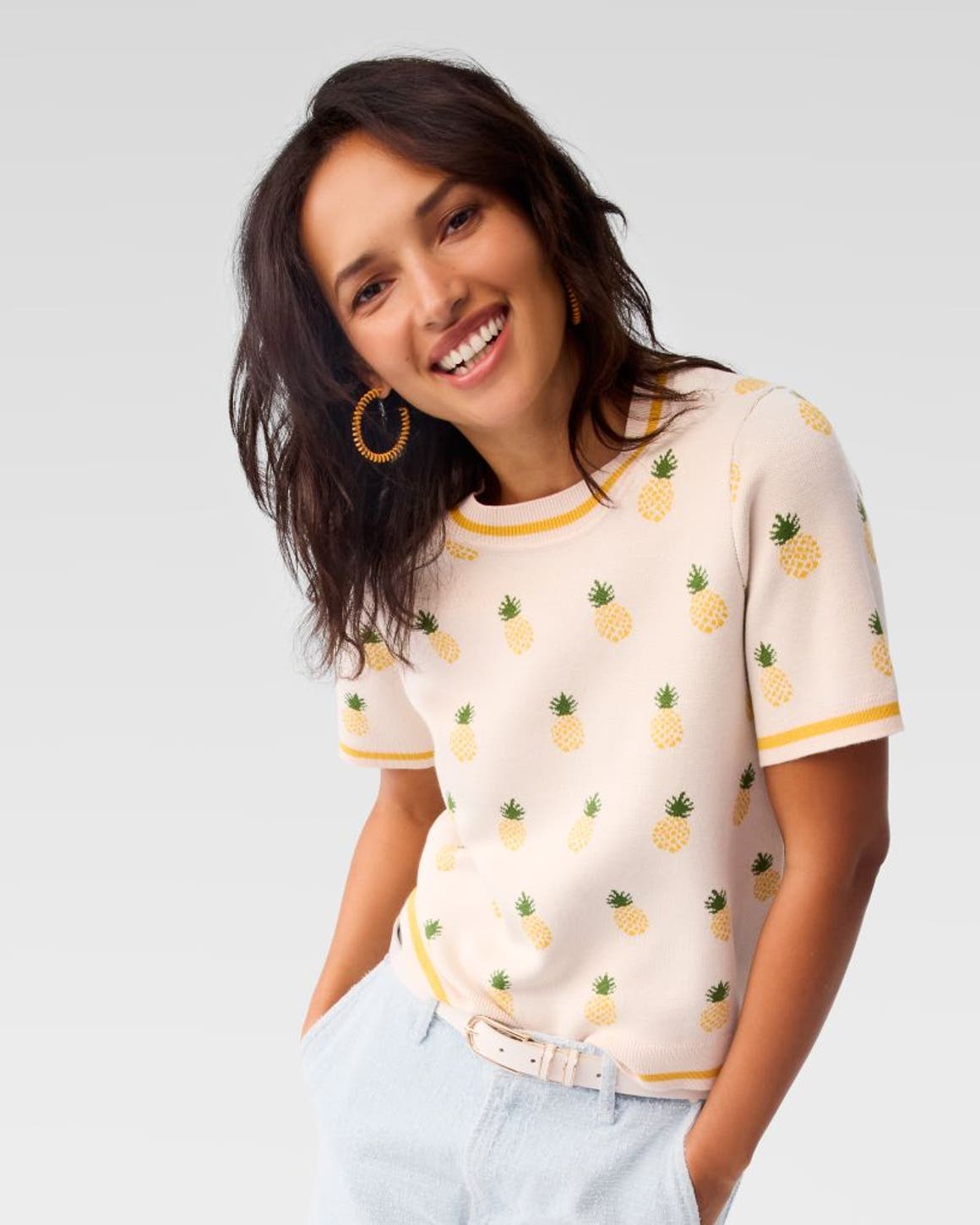 A woman wearing a knit top with a pineapple pattern and blue shorts.