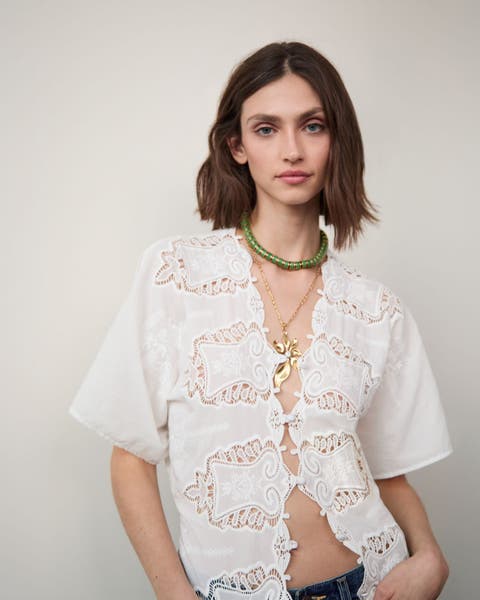 Woman wearing an embroidered top and layered necklaces.