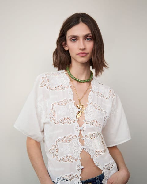 Woman wearing a white lace top and layered necklaces.