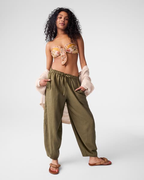 A woman wearing a bikini top, green bottoms and sandals.