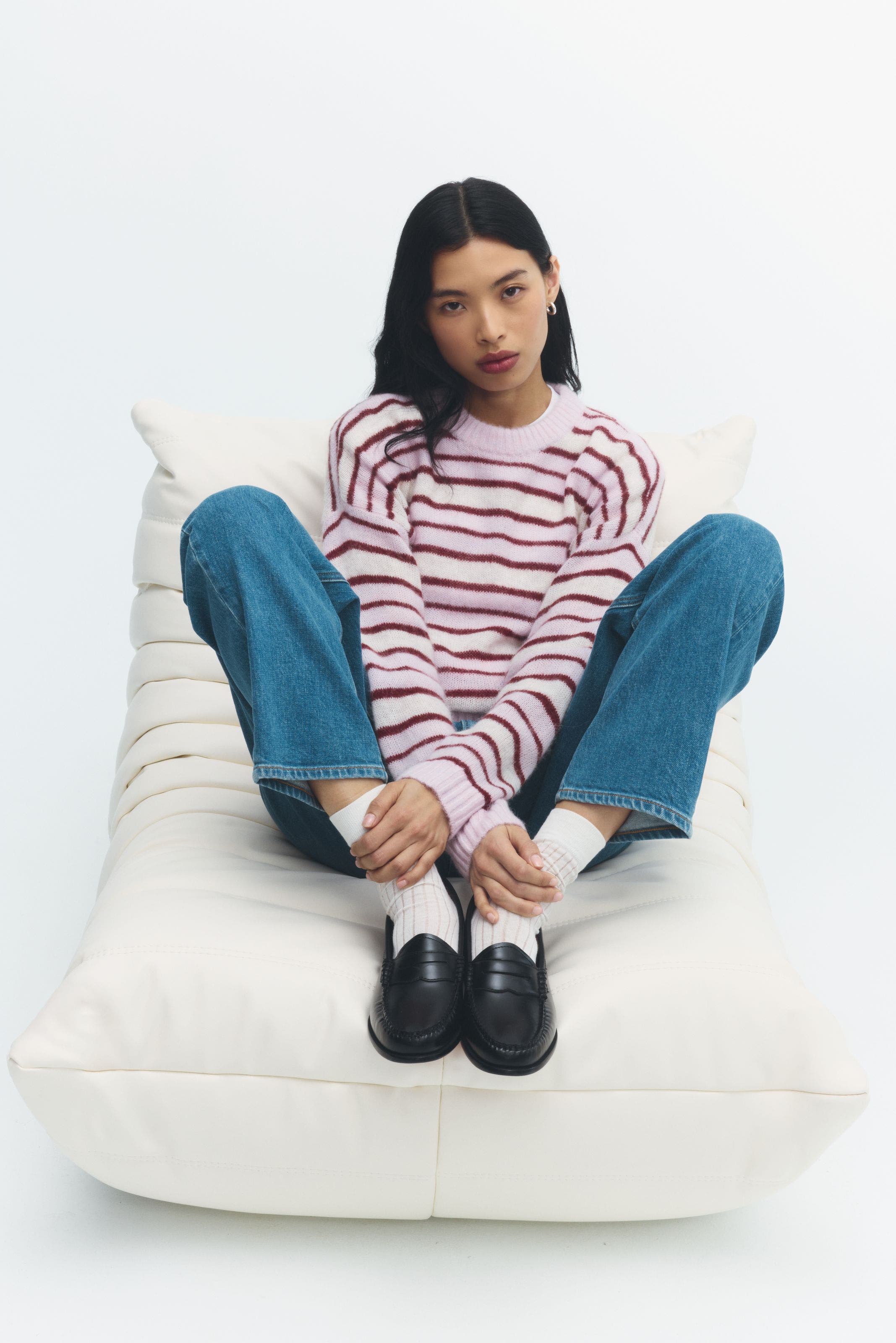 A woman wearing a striped sweater, light wash jeans, and black loafers.