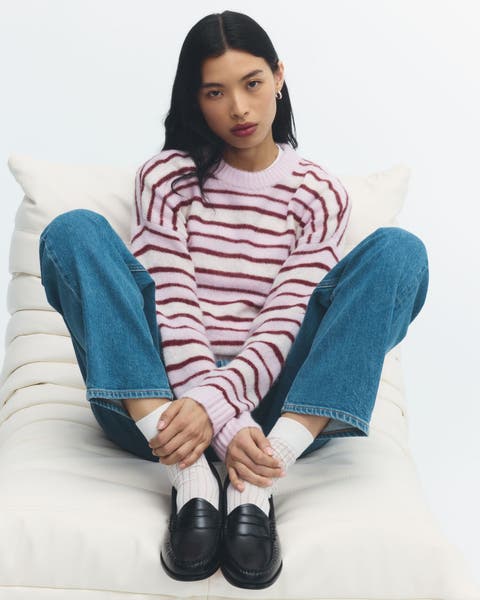 A woman wearing a striped sweater, light wash jeans, and black loafers.