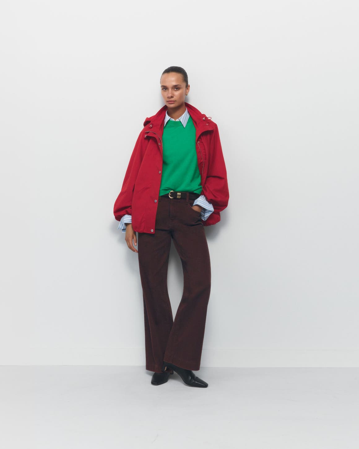 A woman wearing a green sweater and red coat over a button-up with pants and boots.