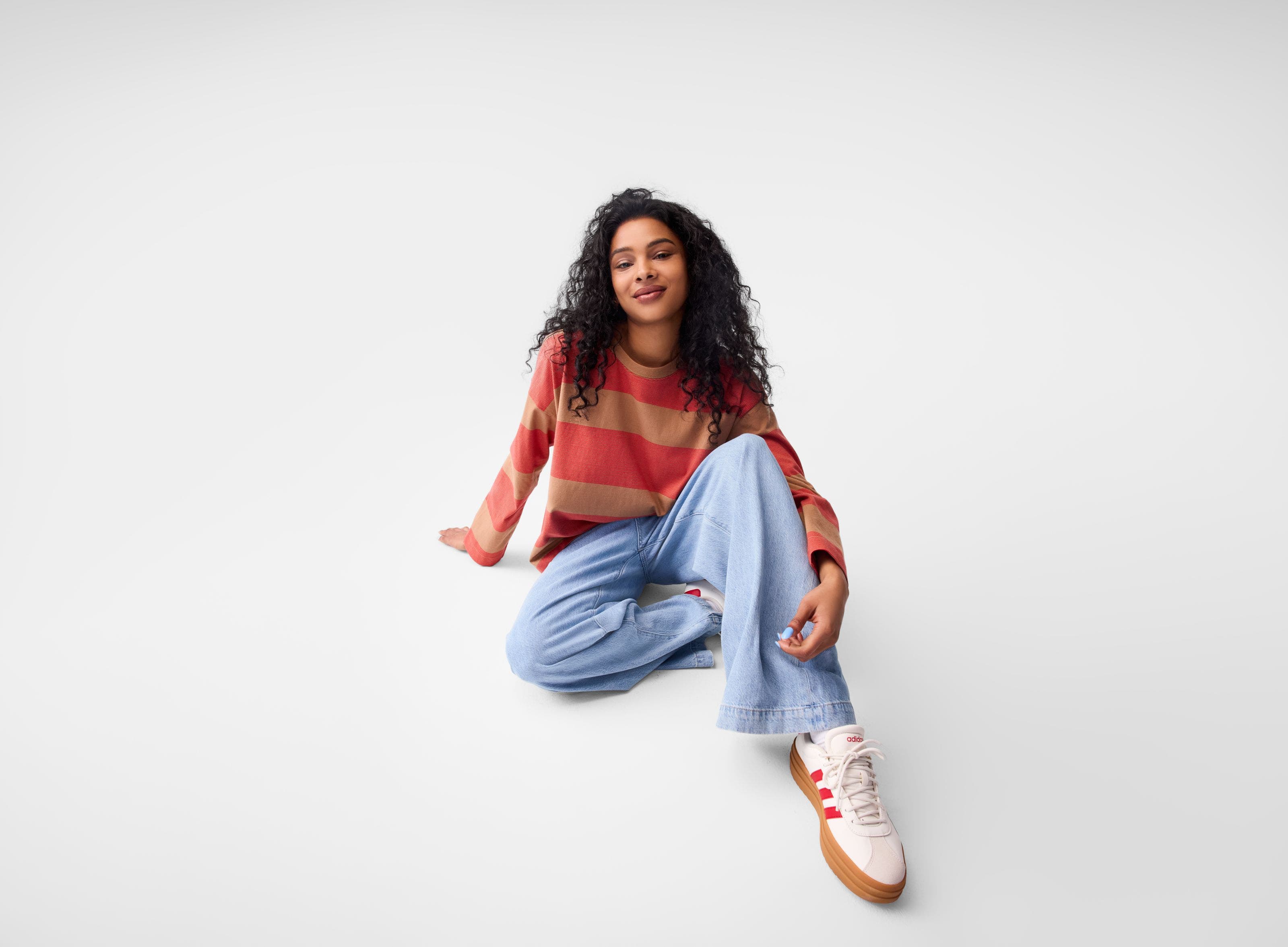 A woman wearing a stripe sweater, jeans and sneakers. 