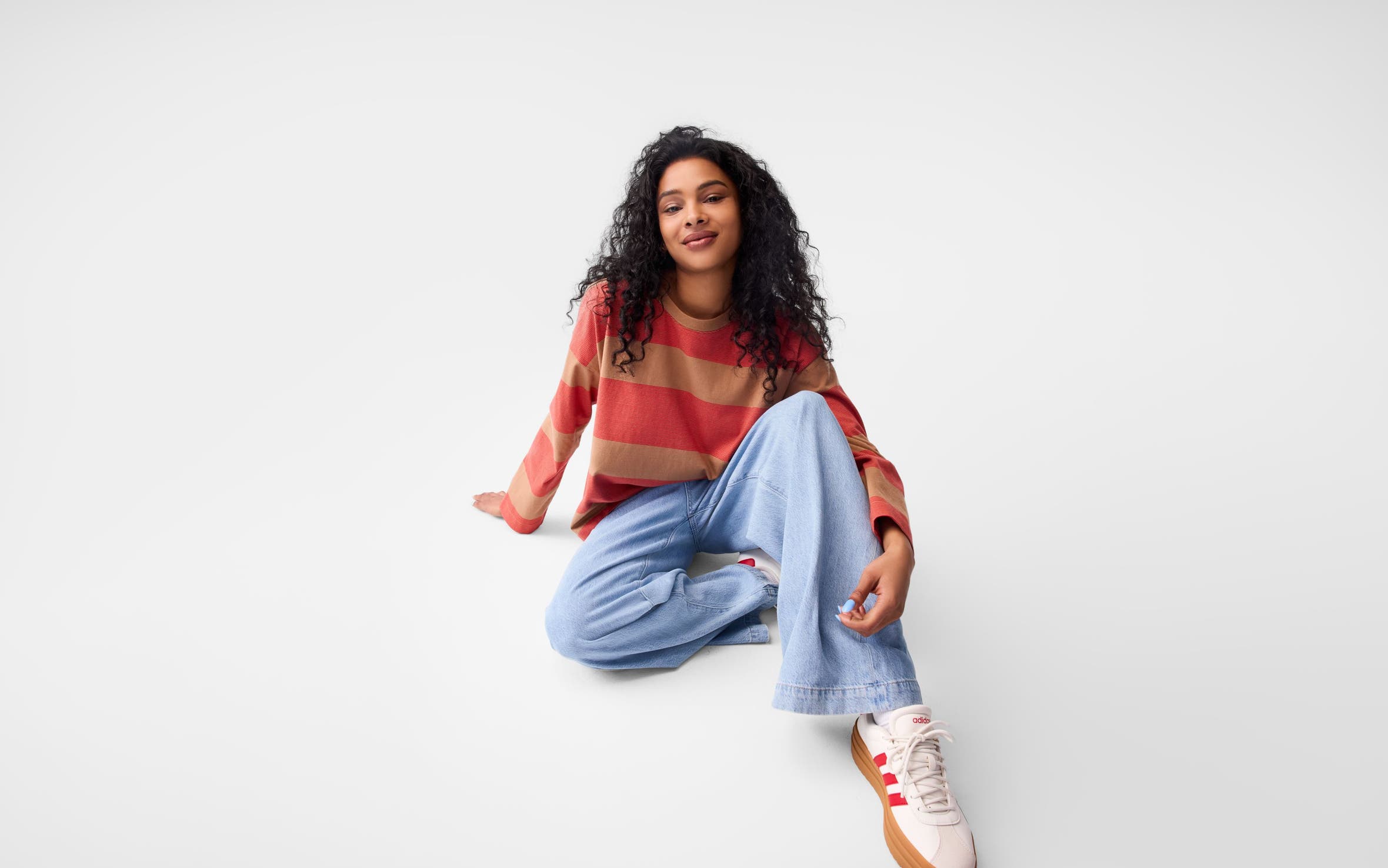 A woman wearing a stripe sweater, jeans and sneakers. 