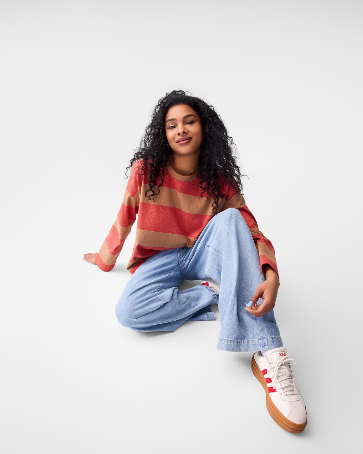 A woman wearing a stripe sweater, jeans and sneakers. 