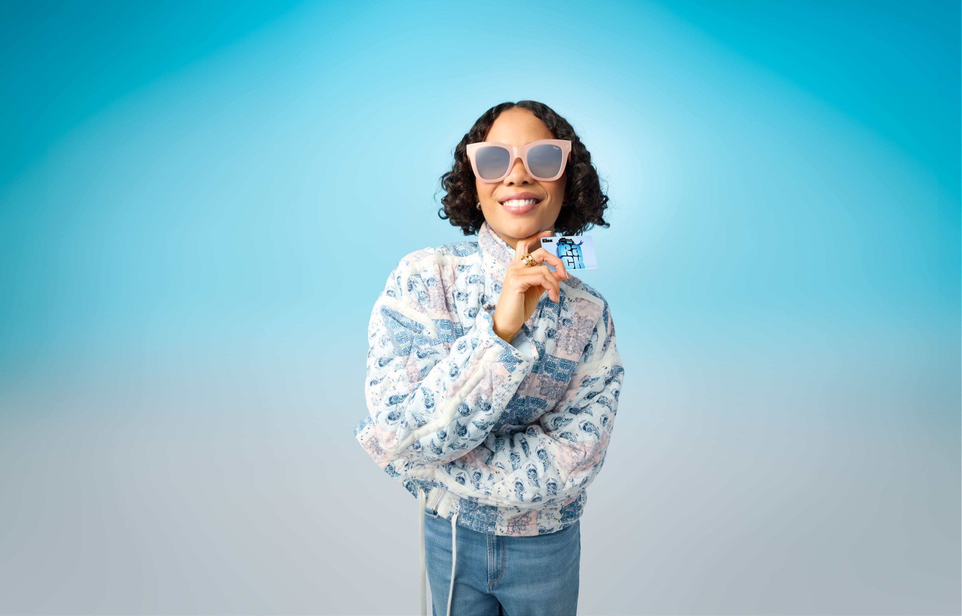 Woman wearing sunglasses and holding a Nordstrom Rack gift card. 