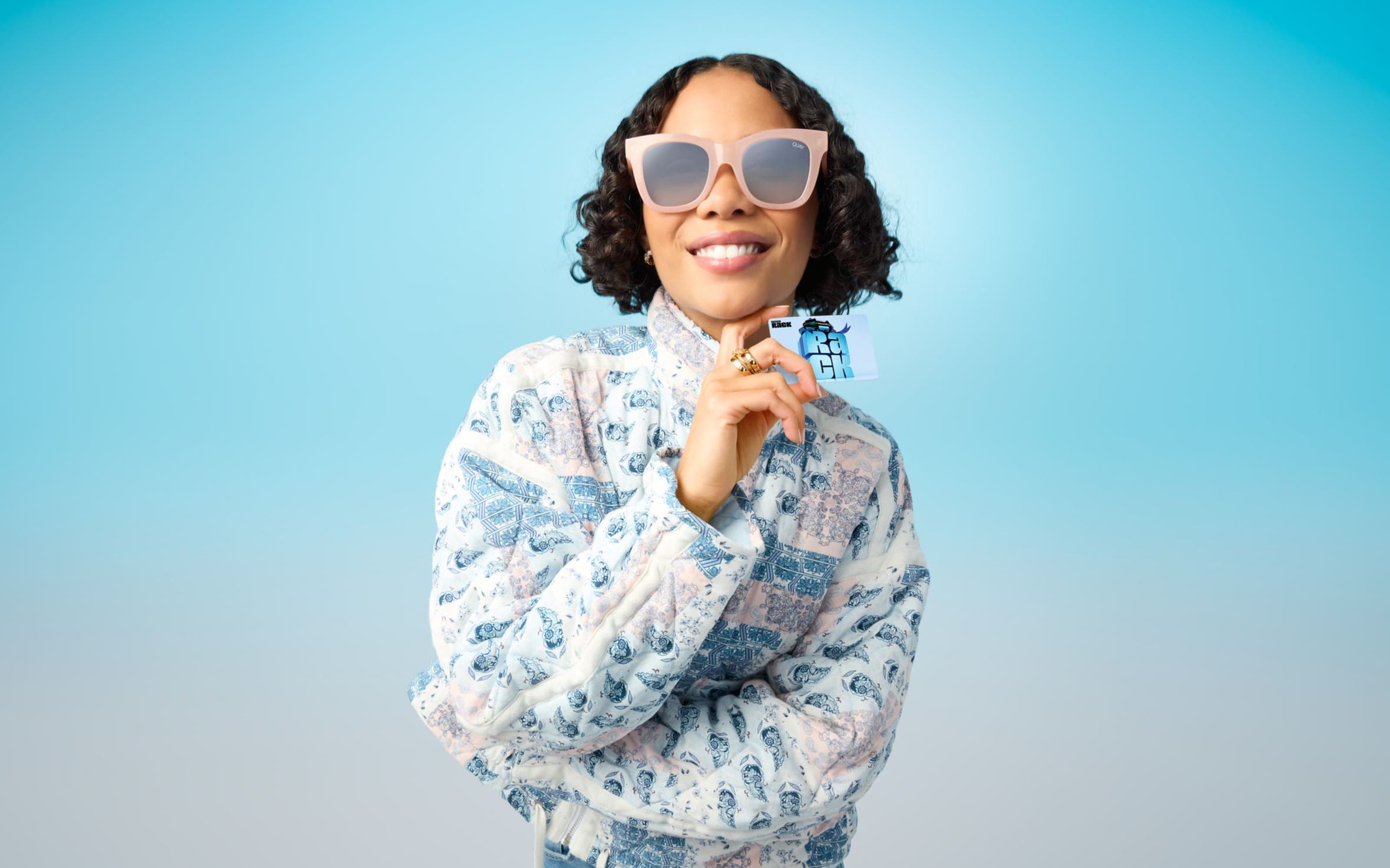 Woman wearing sunglasses and holding a Nordstrom Rack gift card.