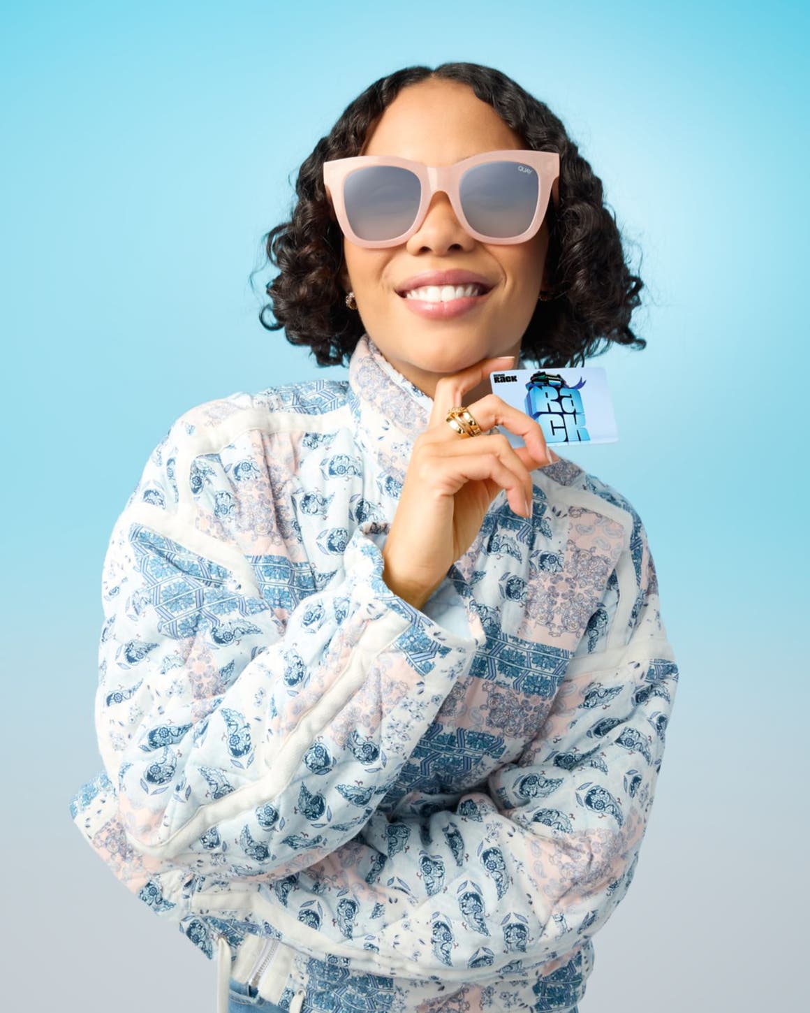 Woman wearing sunglasses and holding a Nordstrom Rack gift card.