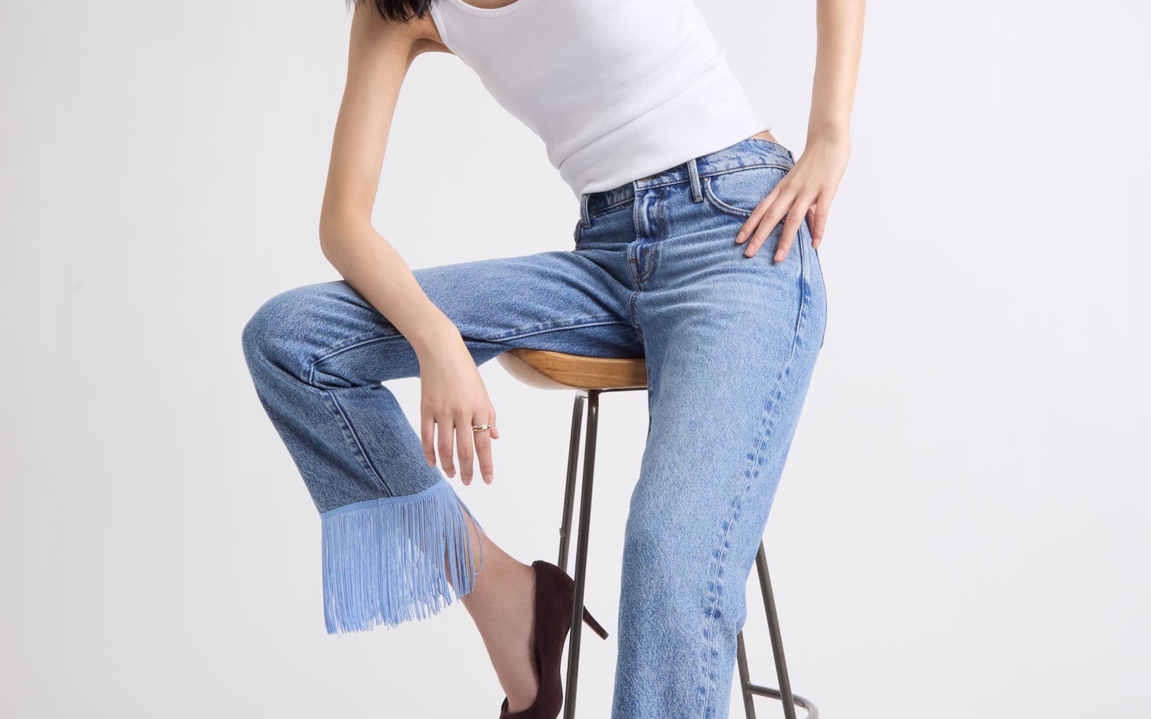 A woman wearing a pair of embellished hemmed denim and a white tank top.
