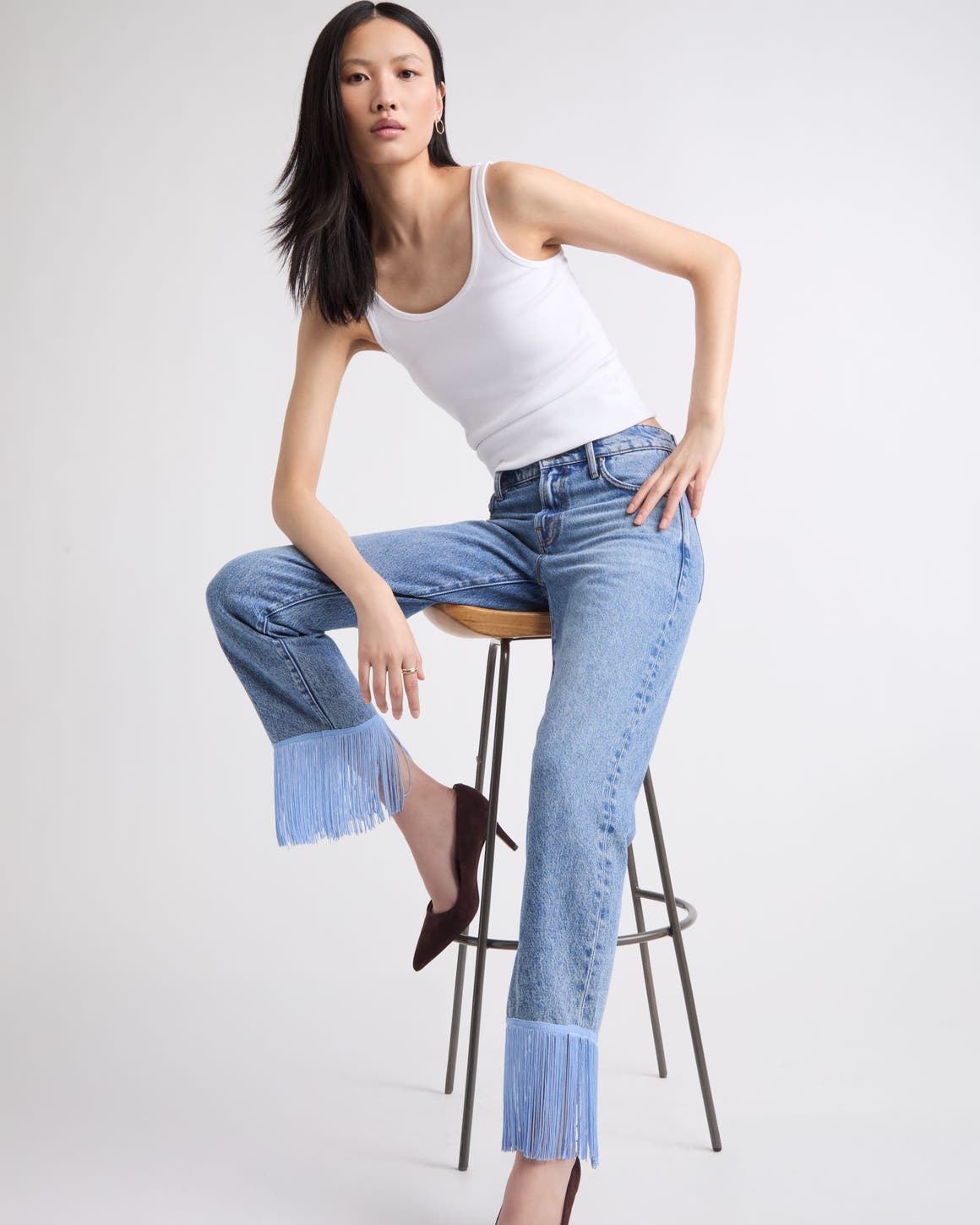 A woman wearing a pair of embellished hemmed denim and a white tank top.