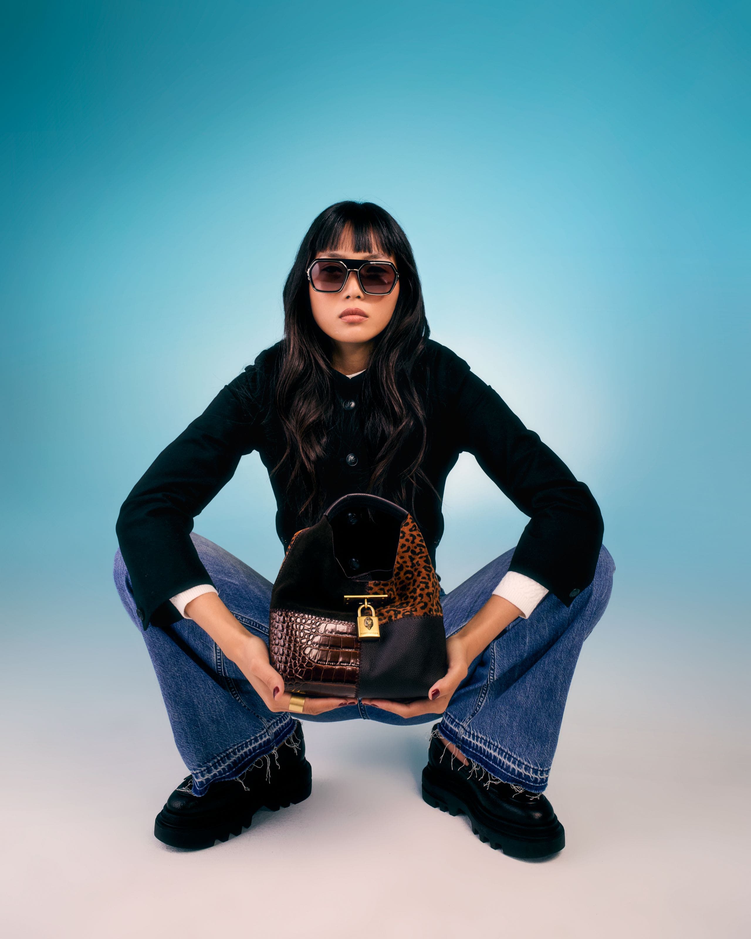 Woman in sunglasses and a black jacket holding a small black handbag with mixed animal textures and gold hardware.