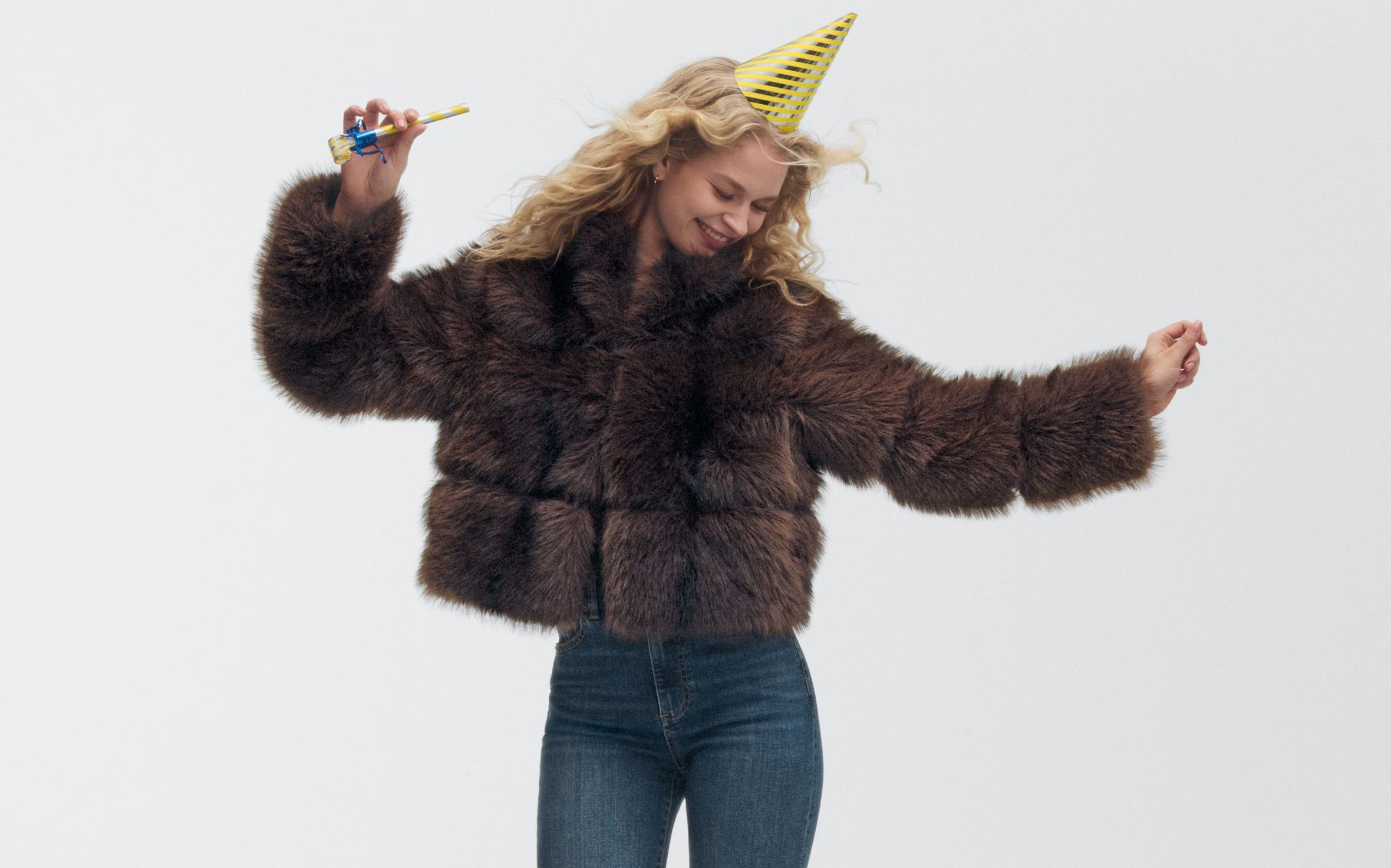 A woman wearing a party hat and faux-fur jacket.