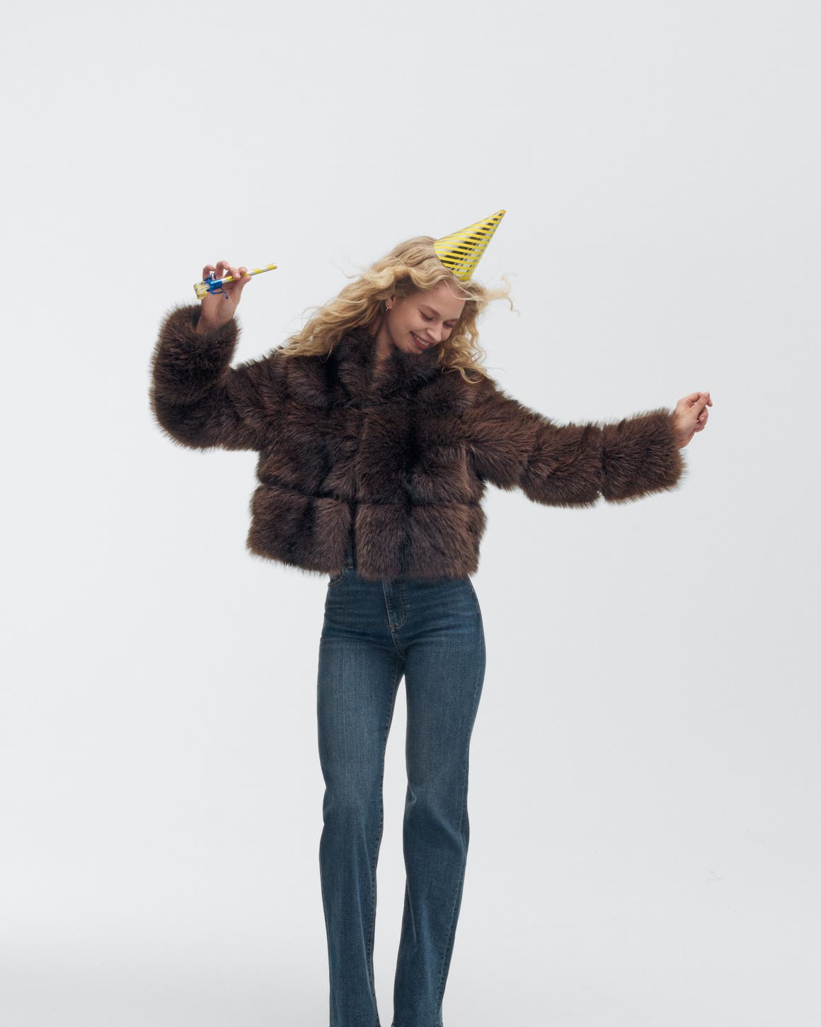 A woman wearing a party hat and faux-fur jacket.