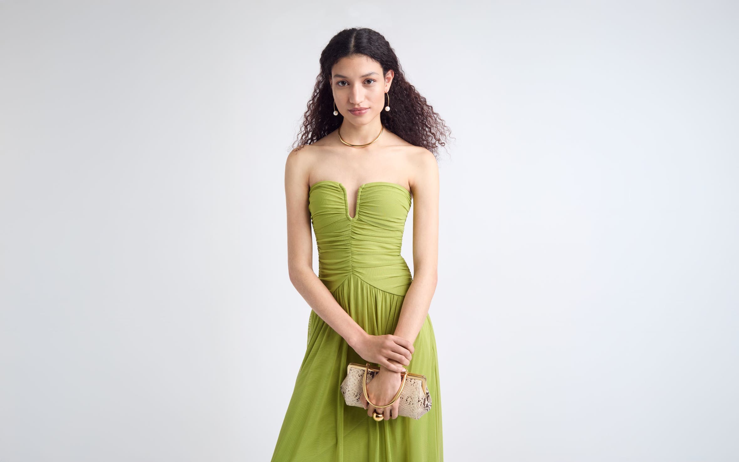 Woman wearing a green strapless gown with jewelry and a clutch.