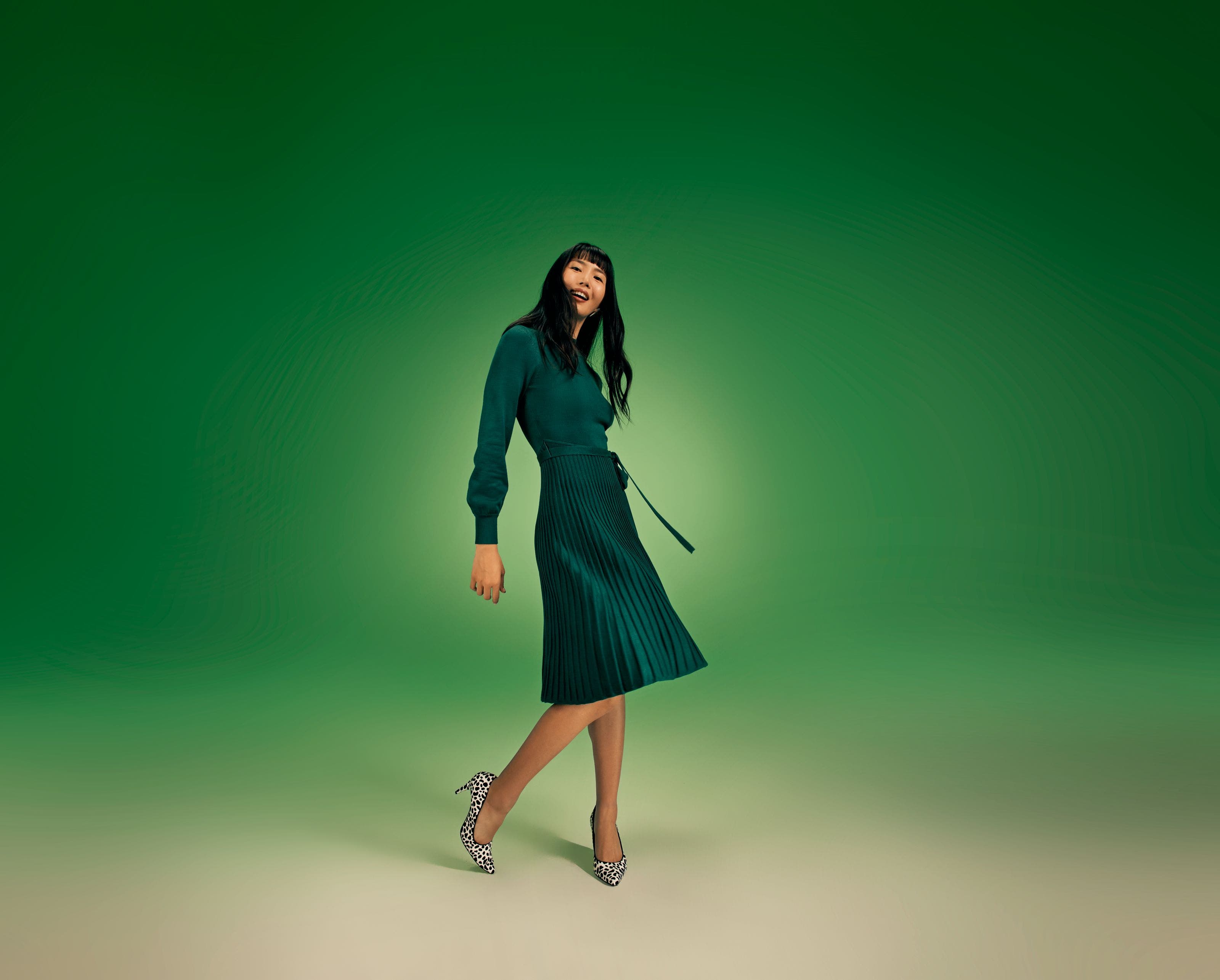 A woman wearing a long-sleeve green dress with a pleated skirt. 