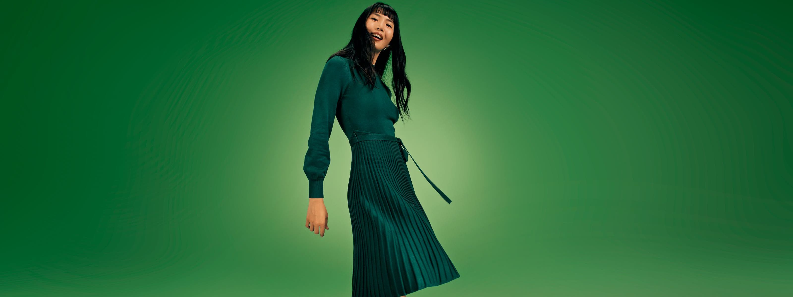 A woman wearing a long-sleeve green dress with a pleated skirt. 