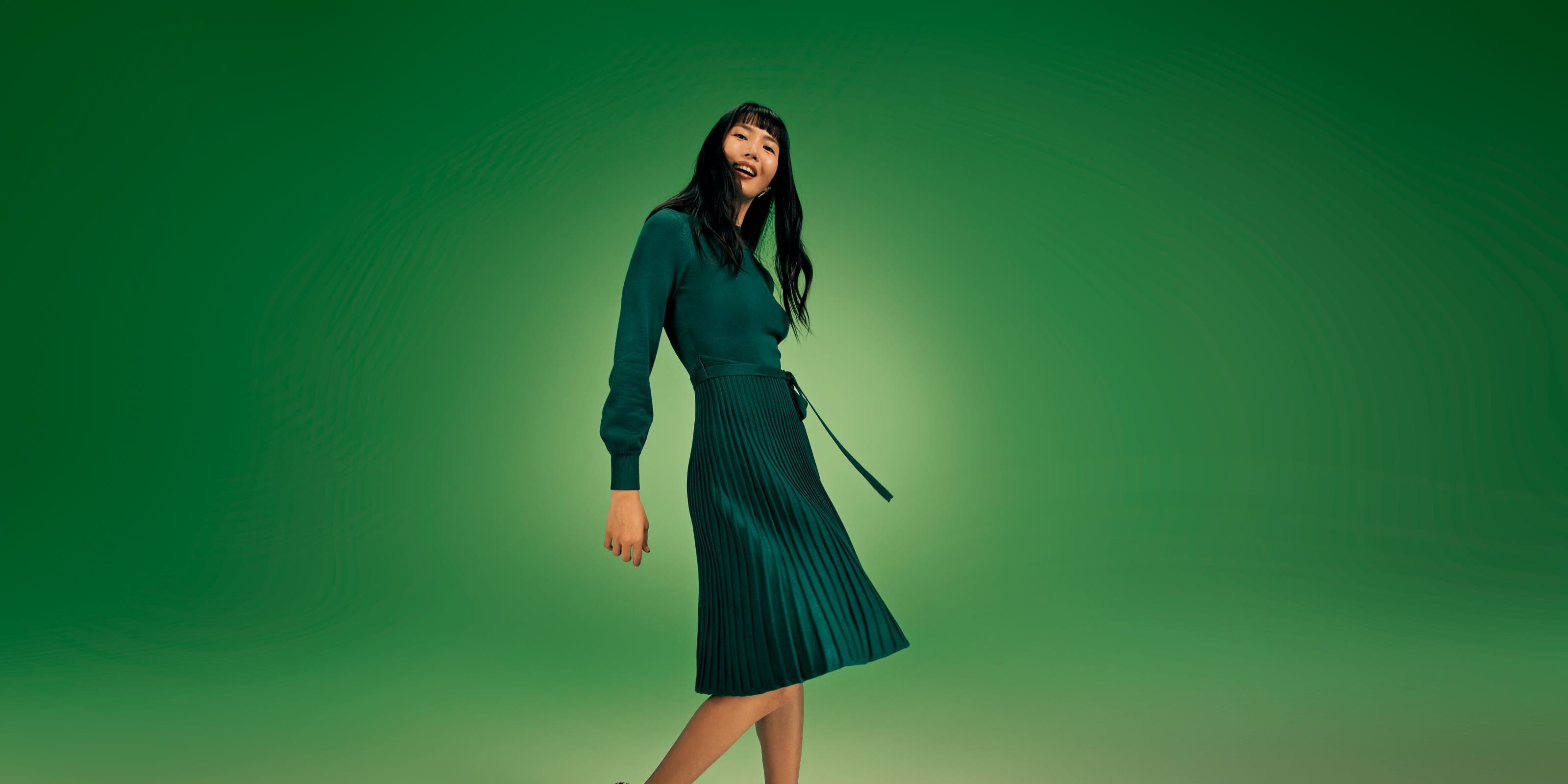 A woman wearing a long-sleeve green dress with a pleated skirt. 