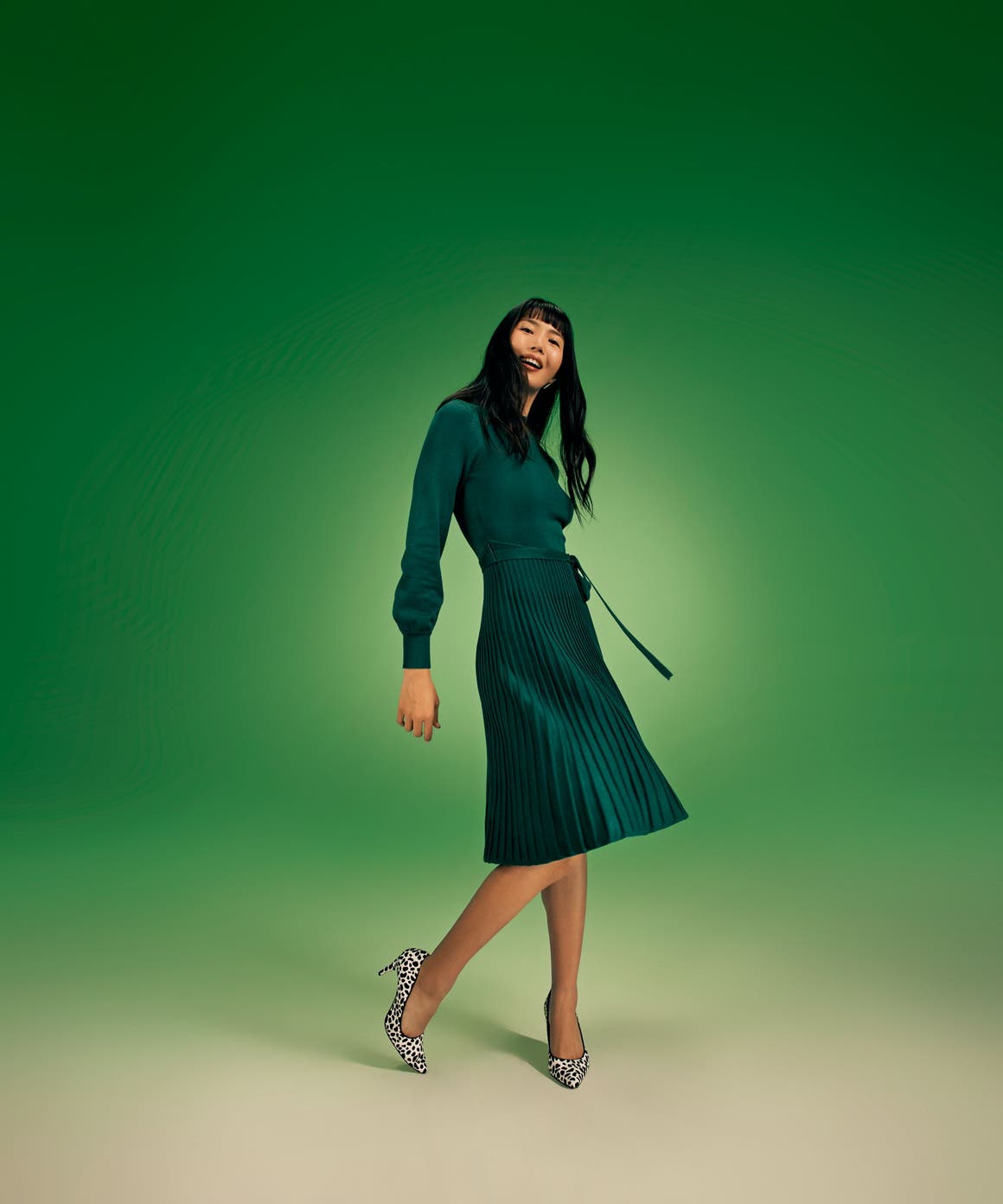 A woman wearing a long-sleeve green dress with a pleated skirt. 