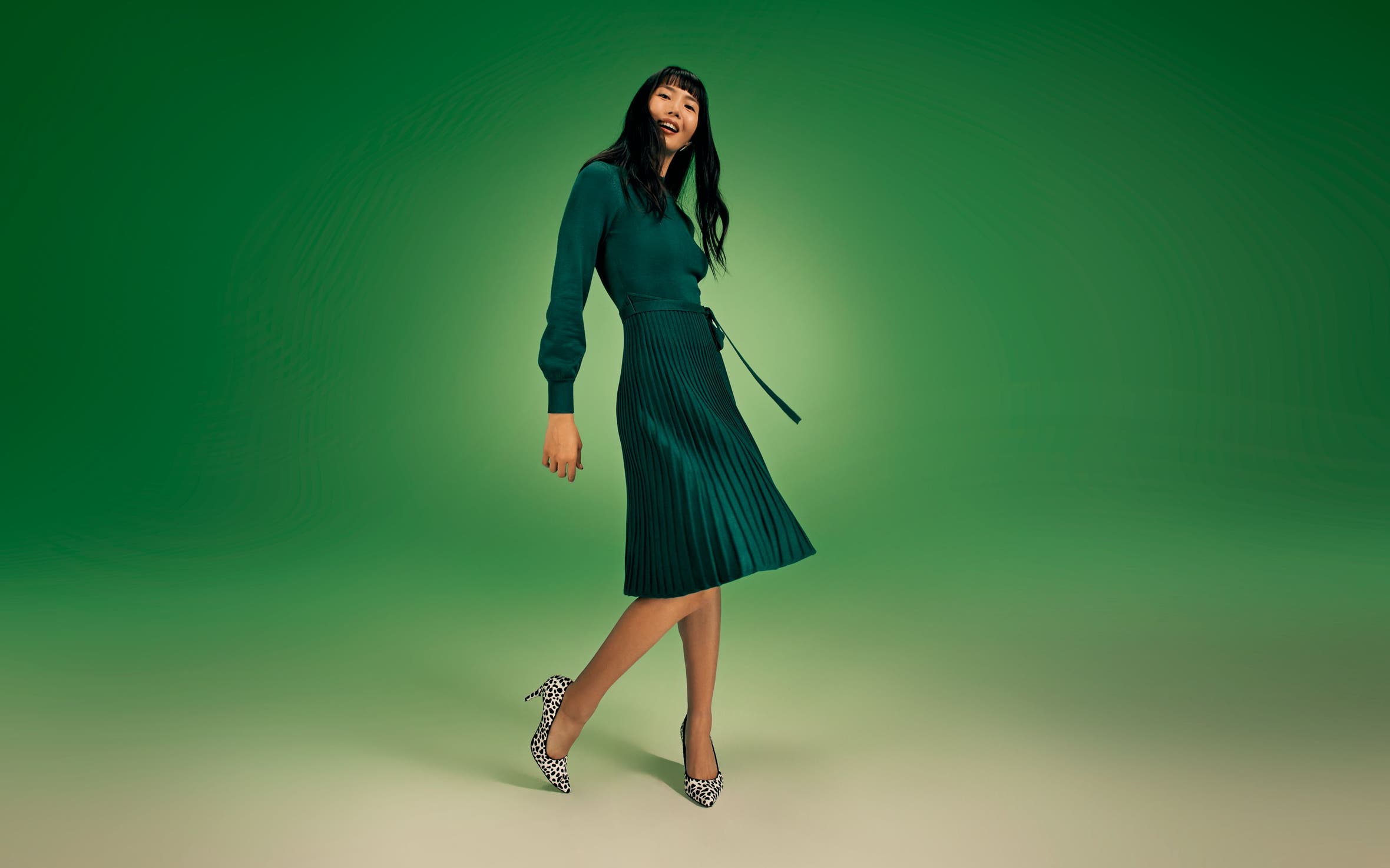 A woman wearing a long-sleeve green dress with a pleated skirt. 