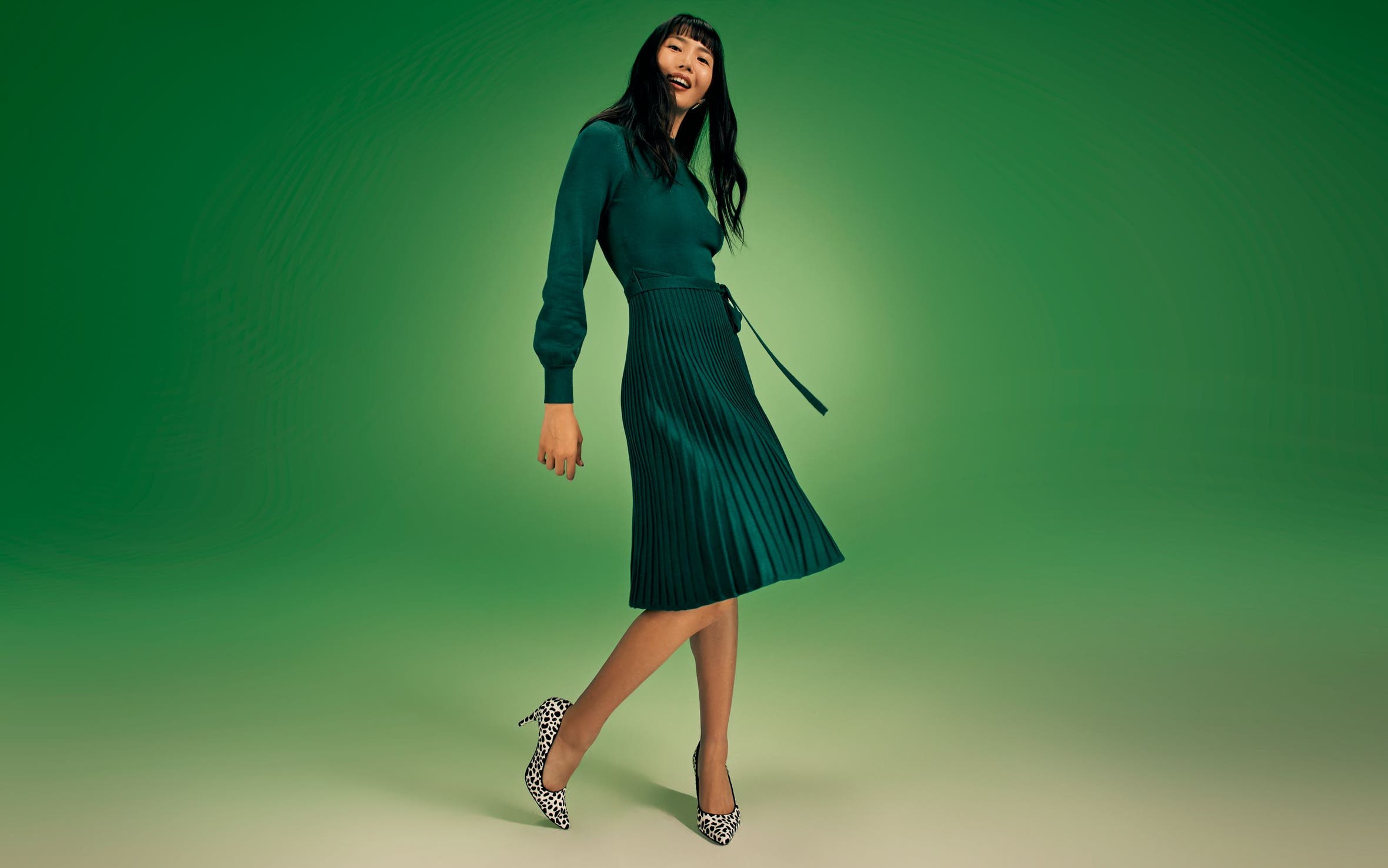 A woman wearing a long-sleeve green dress with a pleated skirt.