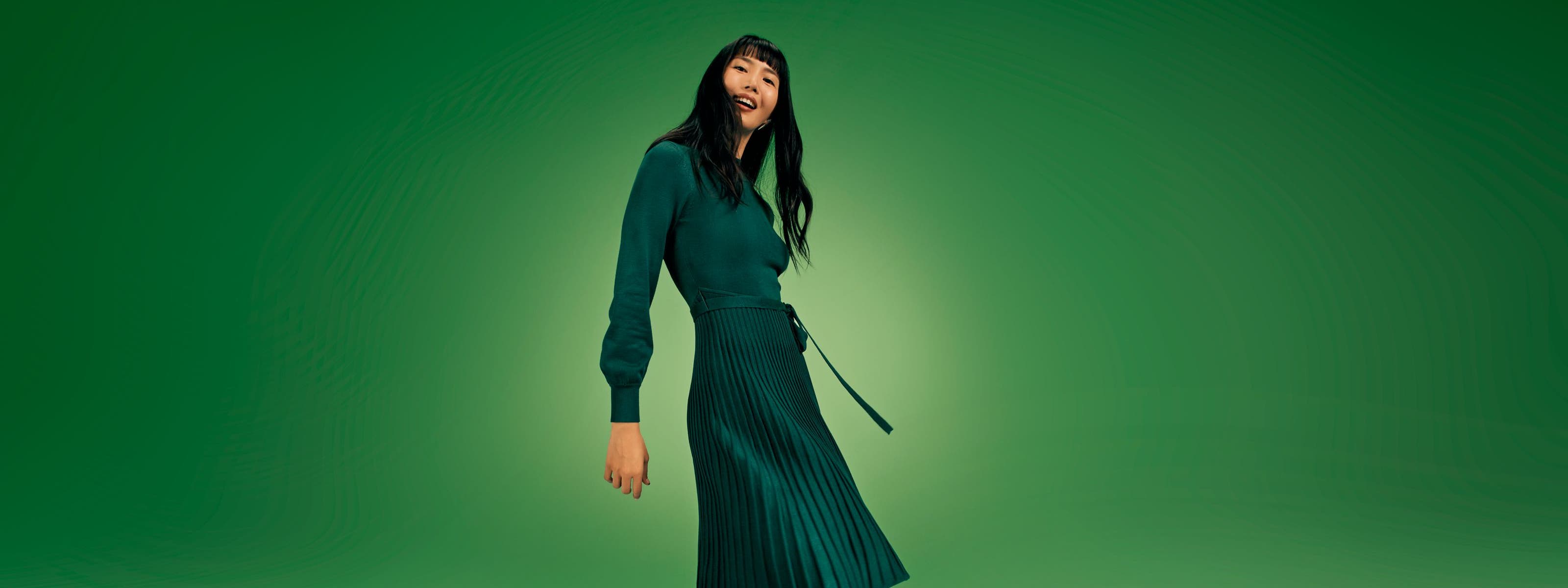 A woman wearing a long-sleeve green dress with a pleated skirt.