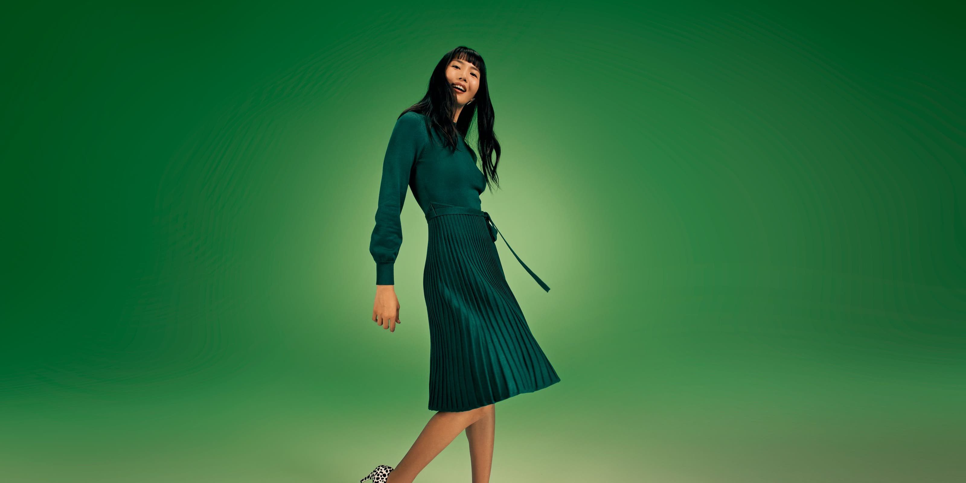 A woman wearing a long-sleeve green dress with a pleated skirt.