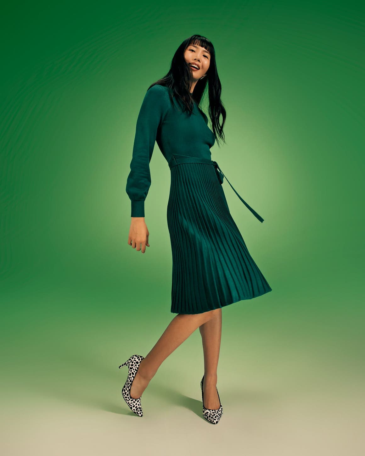 A woman wearing a long-sleeve green dress with a pleated skirt. 
