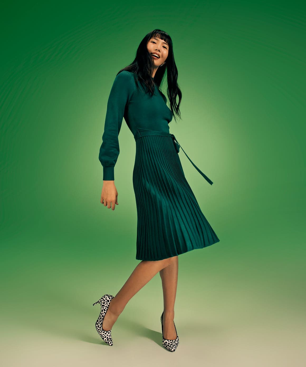A woman wearing a long-sleeve green dress with a pleated skirt.