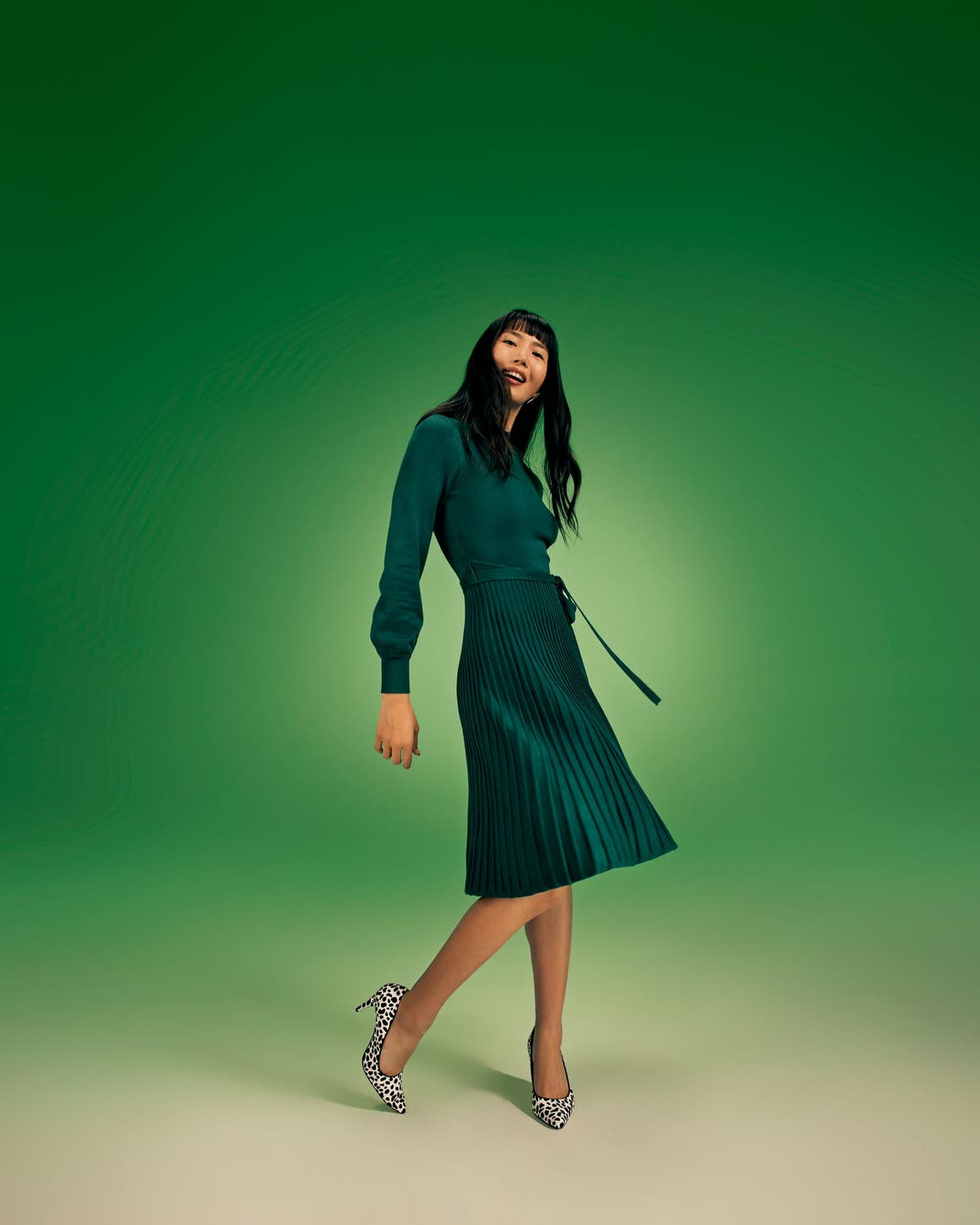 A woman wearing a long-sleeve green dress with a pleated skirt.
