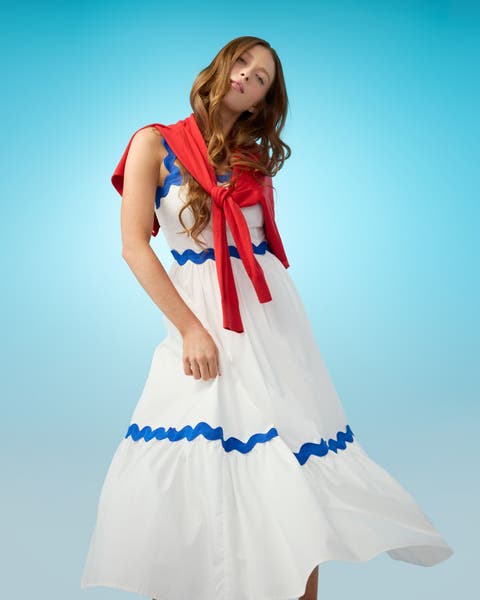 A woman wearing a white dress with a red sweater tied around her shoulders.