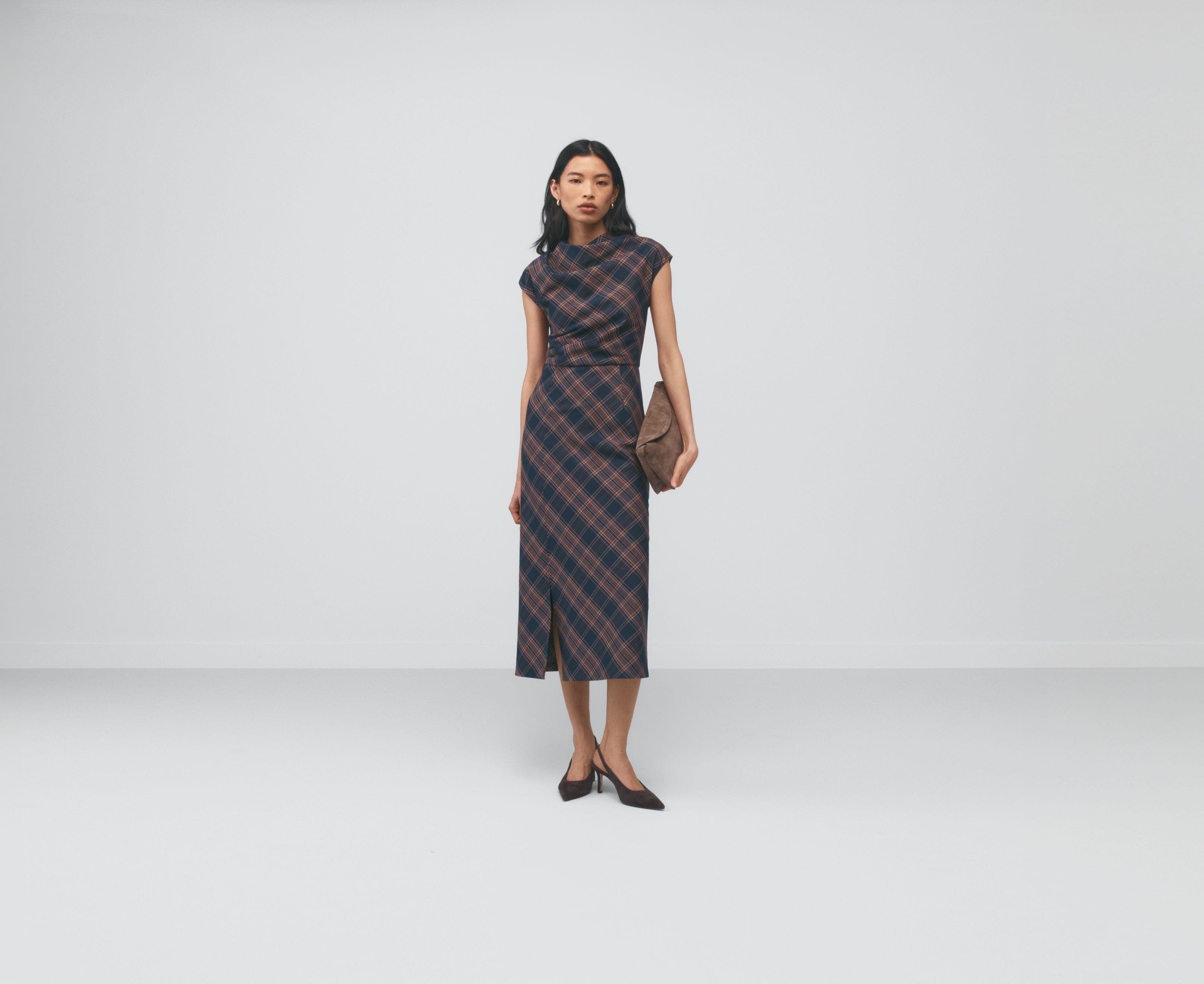 A woman wearing a brown plaid dress holding a handbag.