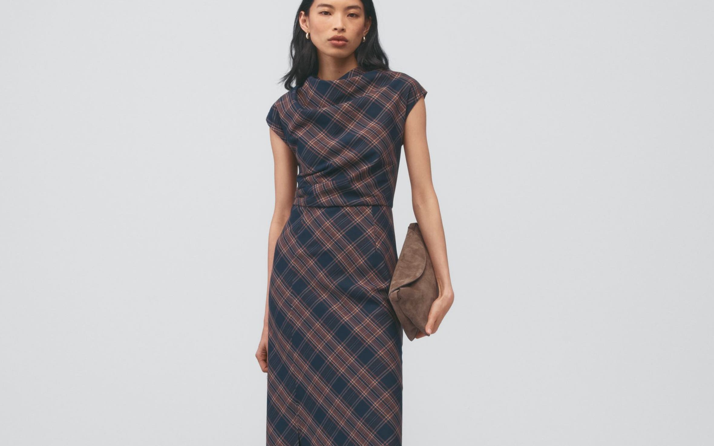 A woman wearing a brown plaid dress holding a handbag.