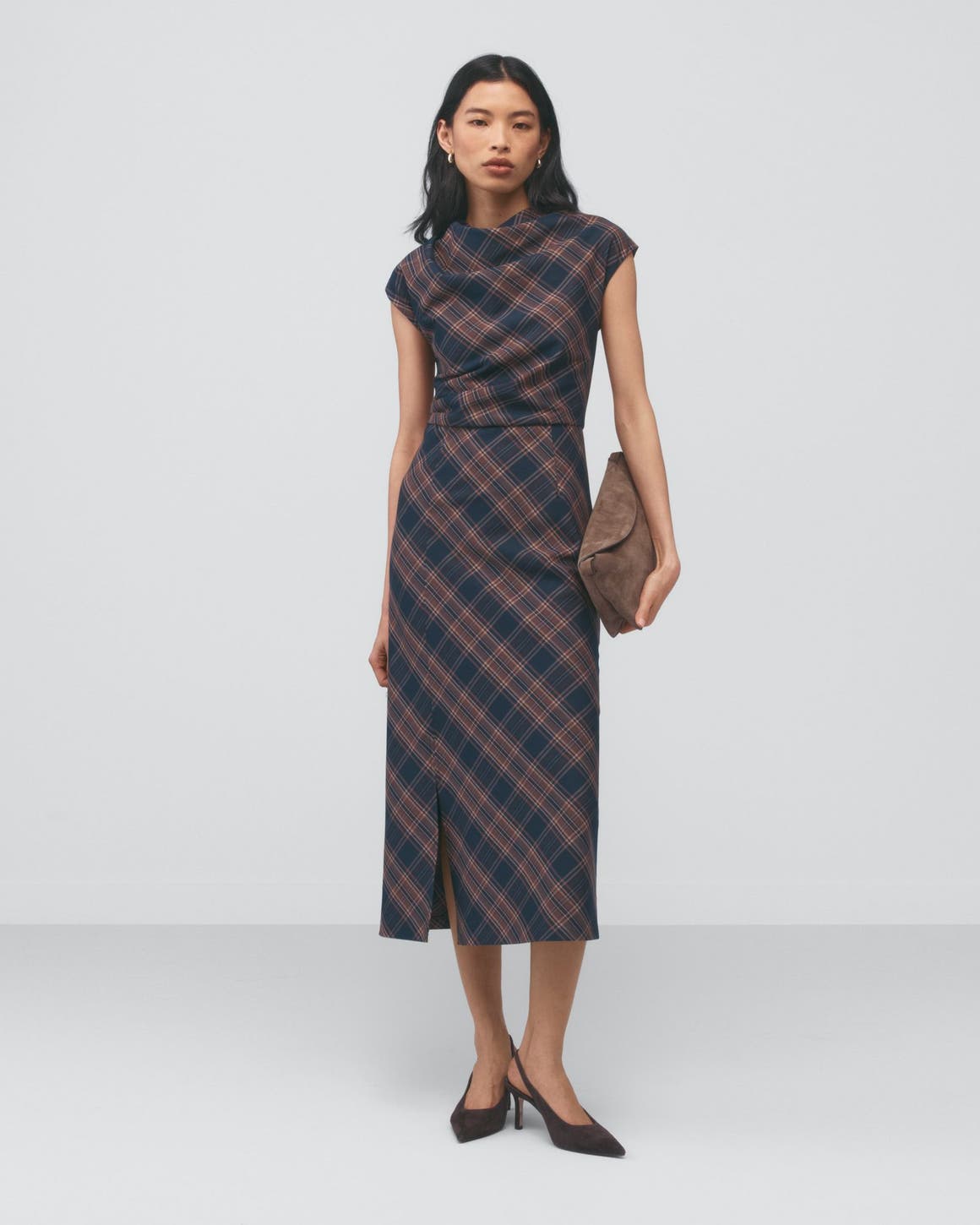 A woman wearing a brown plaid dress holding a handbag.