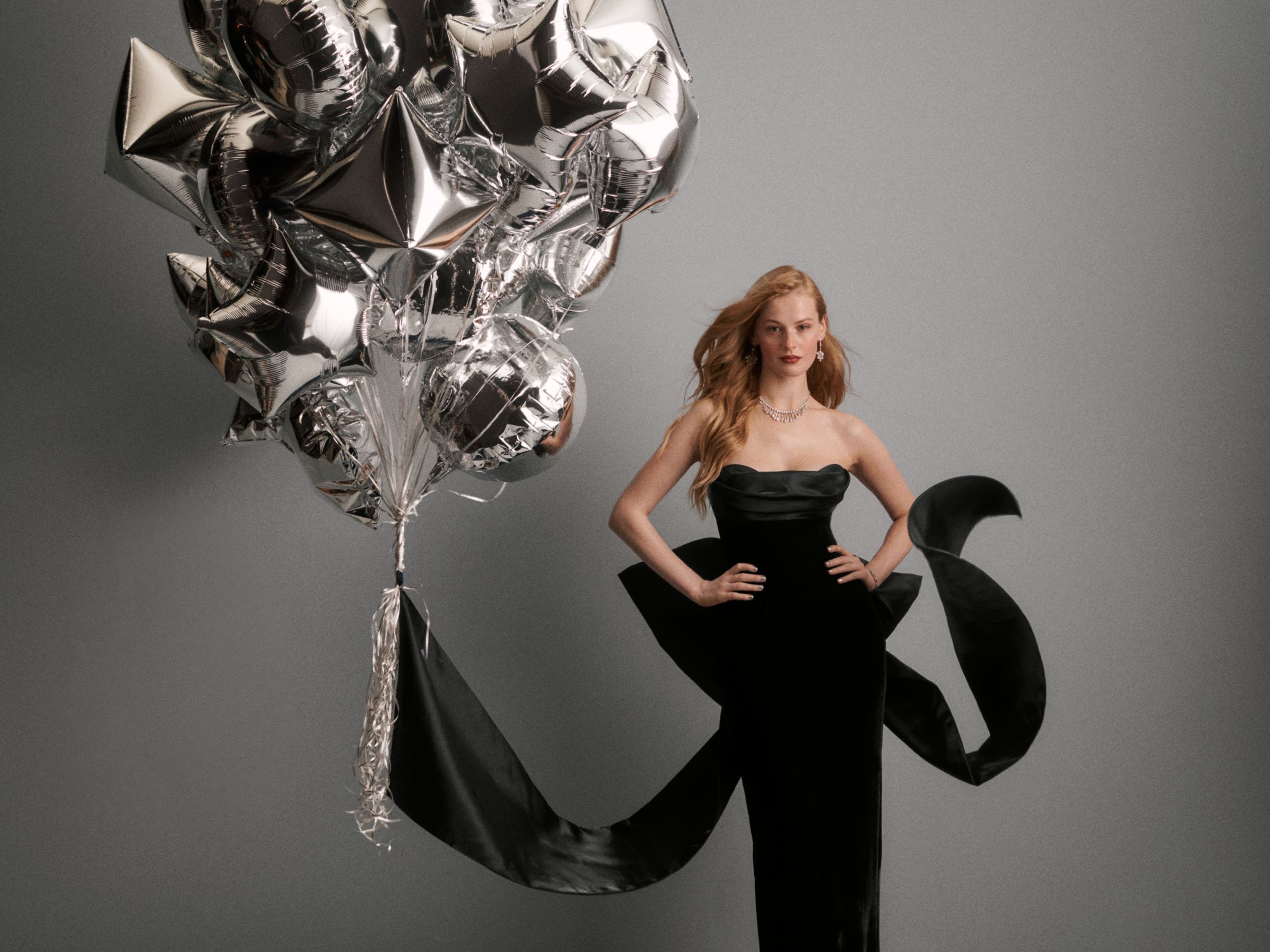 A woman wearing a black gown next to balloons.